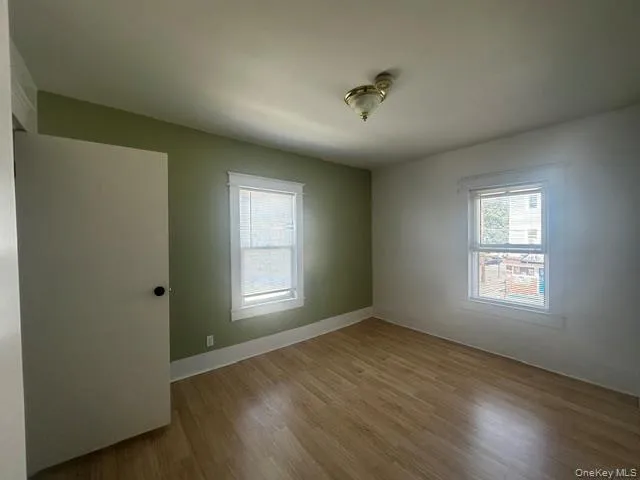 Room featuring wood-finish flooring, two windows with white trim, and a ceiling-mounted light fixture Room featuring wood-finish flooring, two windows with white trim, and a ceiling-mounted light fixture