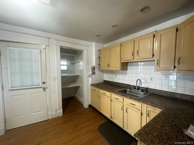 Kitchen featuring wood-finish flooring, recessed lighting, upper and lower cabinetry, a stainless steel sink with a gooseneck faucet, and a tile backsplash Kitchen featuring wood-finish flooring, recessed lighting, upper and lower cabinetry, a stainless steel sink with a gooseneck faucet, and a tile backsplash