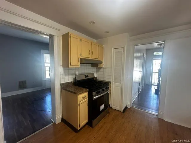 Kitchen featuring wood-finish flooring, granite-style countertops, stainless steel range, and tile backsplash Kitchen featuring wood-finish flooring, granite-style countertops, stainless steel range, and tile backsplash