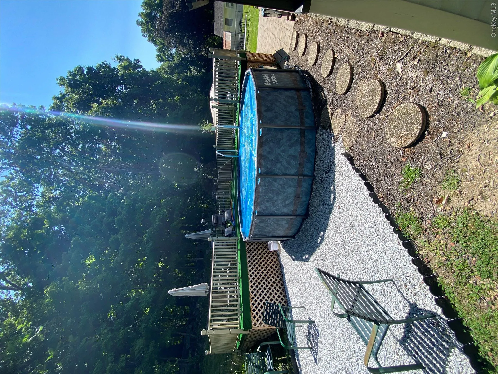 Above-ground pool with surrounding wooden deck, gravel patio area, and stepping stones Above-ground pool with surrounding wooden deck, gravel patio area, and stepping stones