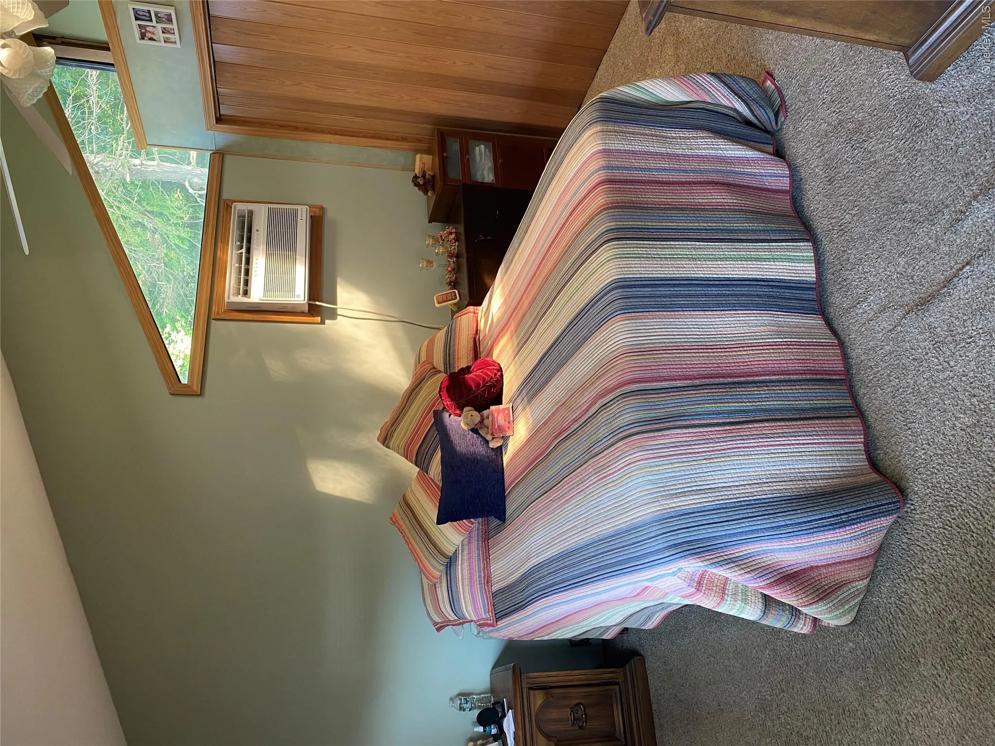 Vaulted ceiling with an accent window, window-mounted air conditioning unit, light-toned carpet flooring, and a folding wood door Vaulted ceiling with an accent window, window-mounted air conditioning unit, light-toned carpet flooring, and a folding wood door