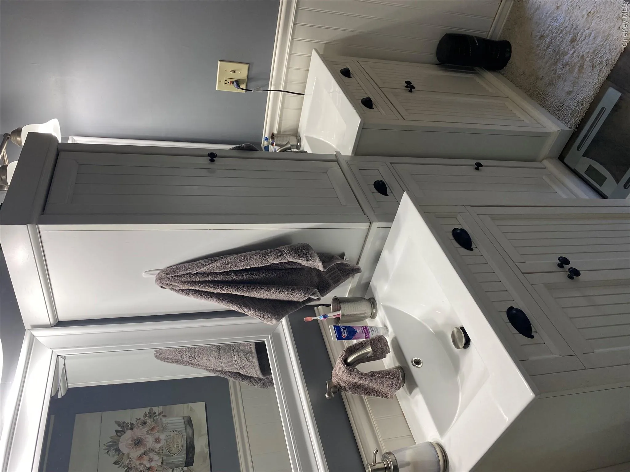 Dual white vanities with beadboard cabinetry, integrated basin sinks, and dark hardware Dual white vanities with beadboard cabinetry, integrated basin sinks, and dark hardware