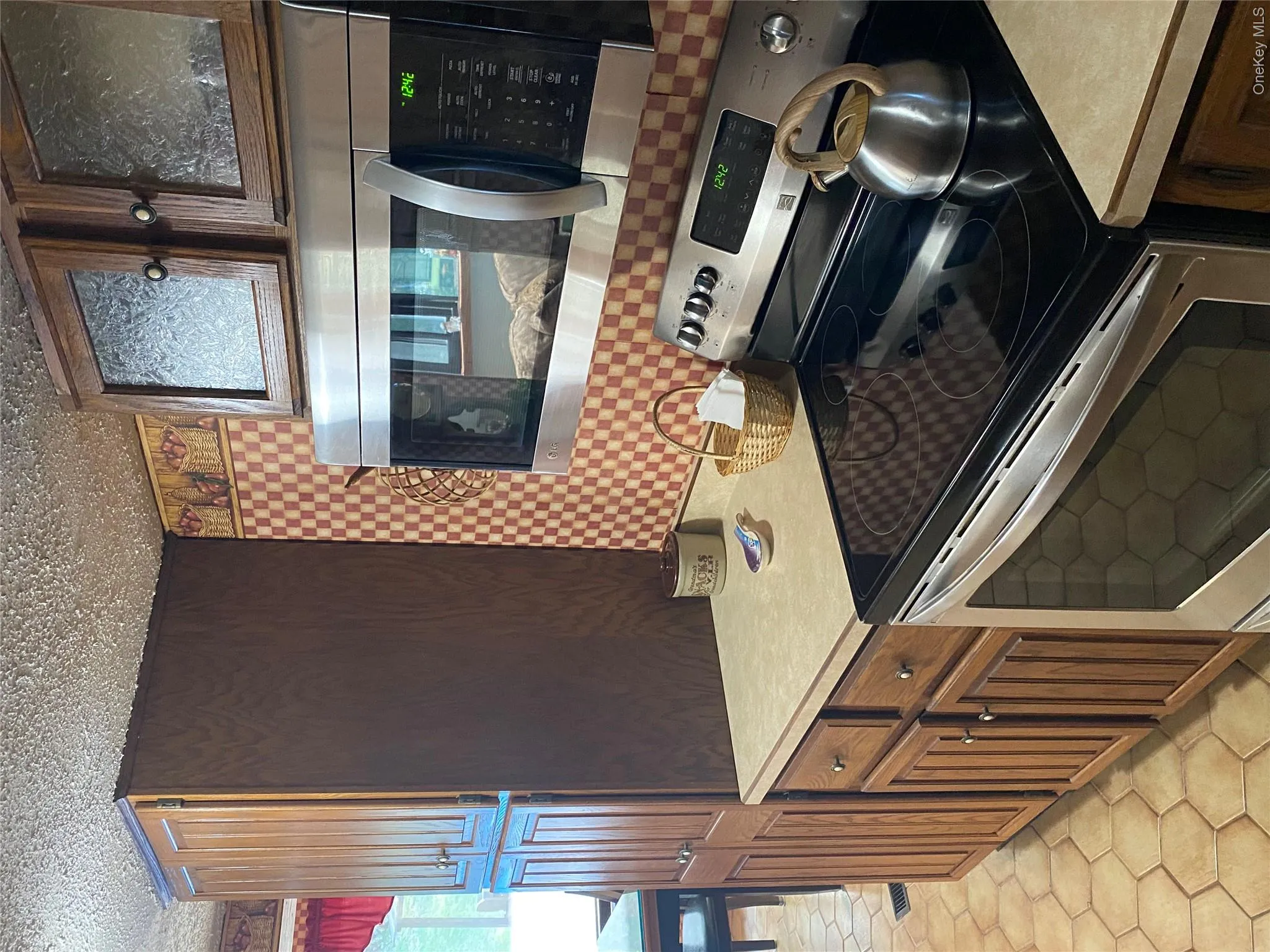 Wood cabinetry with varied door styles, stainless steel microwave, stainless steel electric range, light-toned countertop, and hexagonal tile flooring Wood cabinetry with varied door styles, stainless steel microwave, stainless steel electric range, light-toned countertop, and hexagonal tile flooring