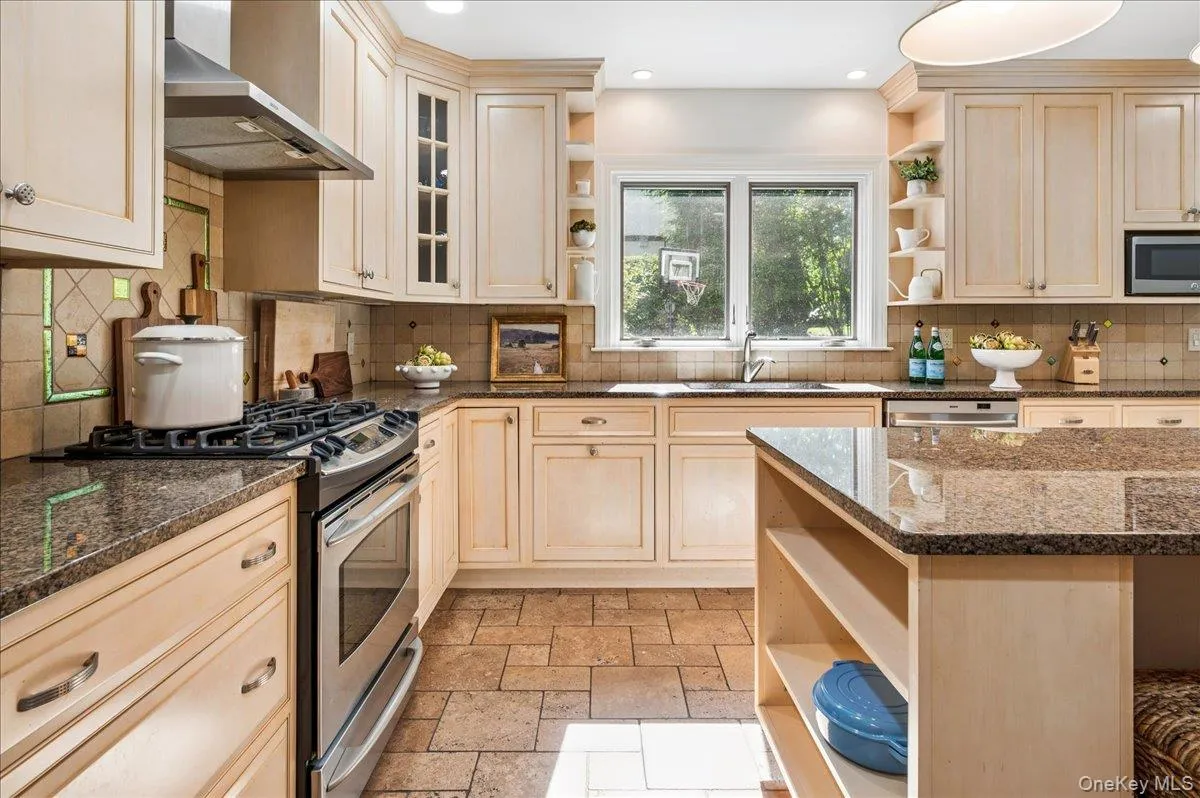Kitchen featuring light wood cabinetry, stone countertops, stainless steel appliances, tile flooring, and a central island with integrated shelving Kitchen featuring light wood cabinetry, stone countertops, stainless steel appliances, tile flooring, and a central island with integrated shelving
