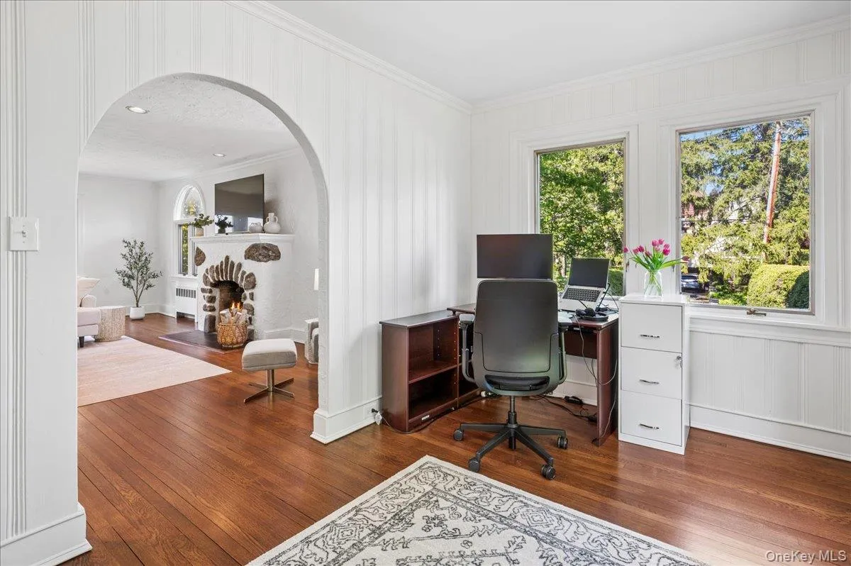 Hardwood flooring in a versatile study, featuring an arched doorway opening to a living area with a stone fireplace Hardwood flooring in a versatile study, featuring an arched doorway opening to a living area with a stone fireplace