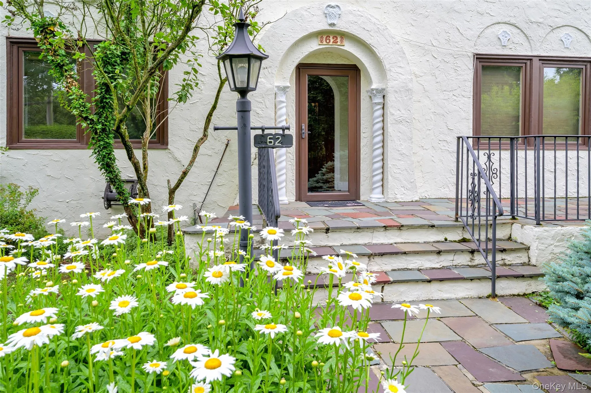 Stucco exterior featuring an arched entryway with decorative pillars, a multi-hued flagstone walkway, and an ornamental wrought iron railing Stucco exterior featuring an arched entryway with decorative pillars, a multi-hued flagstone walkway, and an ornamental wrought iron railing
