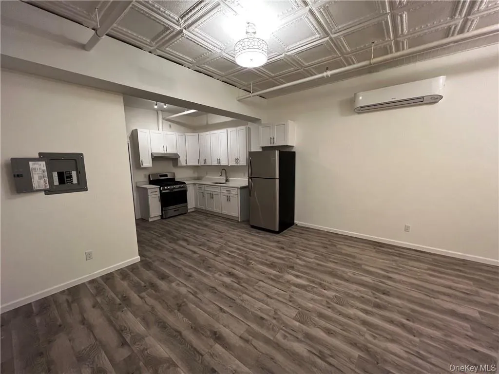 Kitchen with appliances with stainless steel finishes, a wall mounted AC, dark wood-type flooring, sink, and white cabinetry Kitchen with appliances with stainless steel finishes, a wall mounted AC, dark wood-type flooring, sink, and white cabinetry