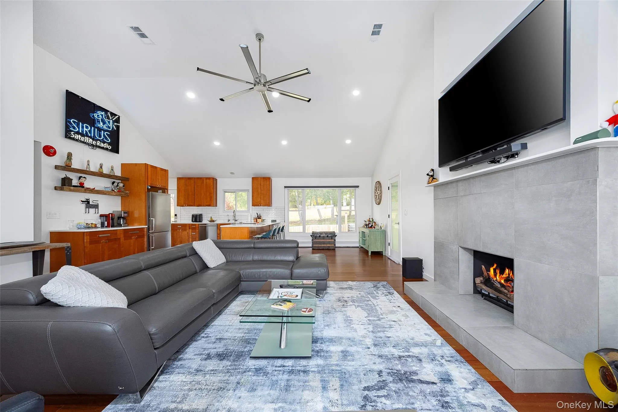 Living area featuring dark wood-style flooring, a tiled fireplace, high vaulted ceiling, recessed lighting, and a ceiling fan Living area featuring dark wood-style flooring, a tiled fireplace, high vaulted ceiling, recessed lighting, and a ceiling fan