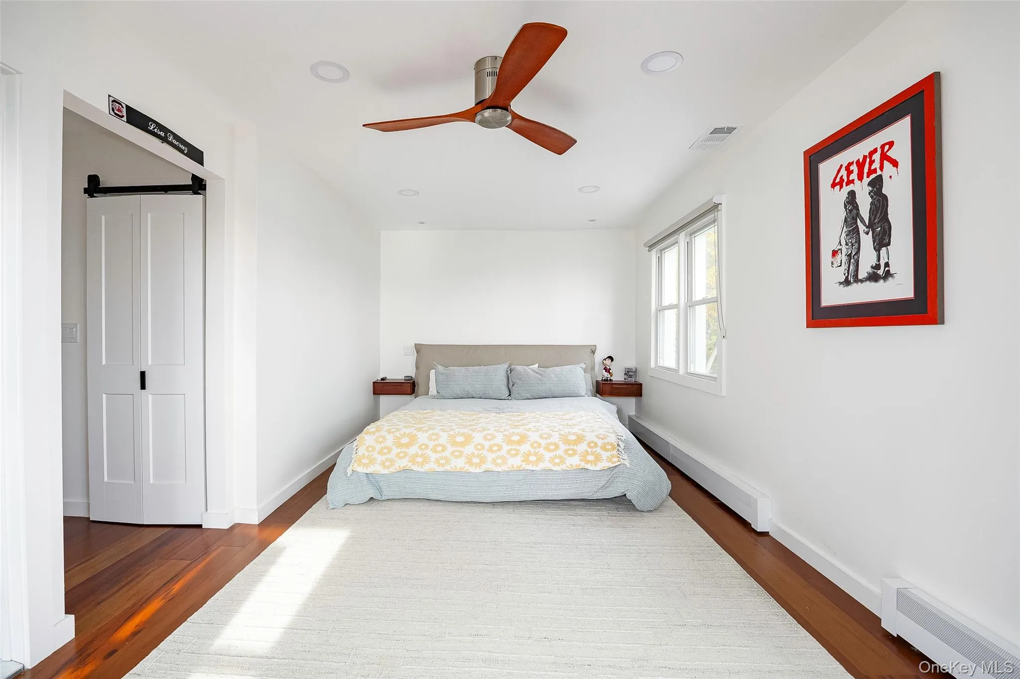 Bedroom featuring a barn door, a baseboard radiator, recessed lighting, wood finished floors, and a ceiling fan Bedroom featuring a barn door, a baseboard radiator, recessed lighting, wood finished floors, and a ceiling fan