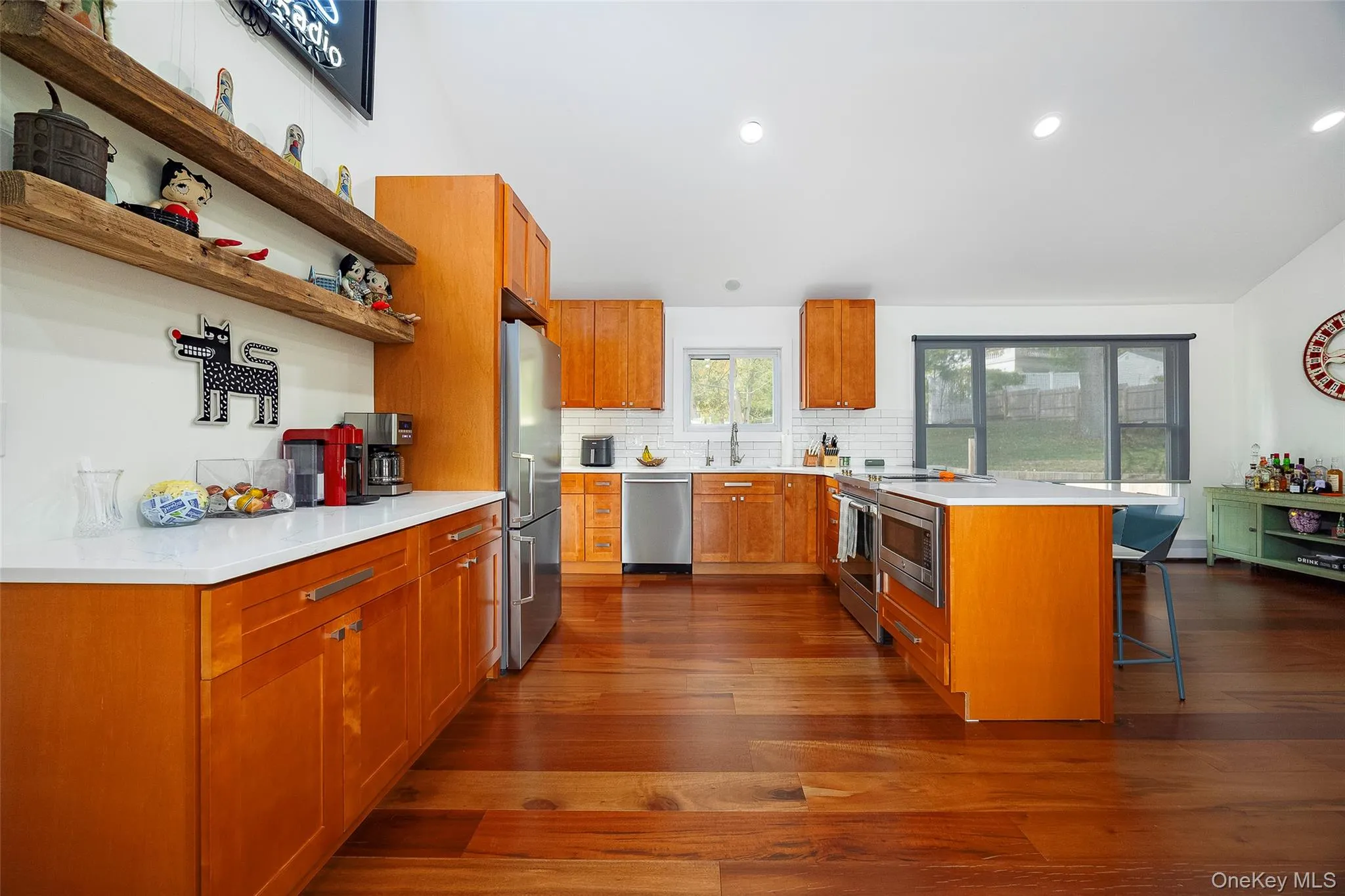 Kitchen with a breakfast bar area, brown cabinets, tasteful backsplash, dark wood-style flooring, and recessed lighting Kitchen with a breakfast bar area, brown cabinets, tasteful backsplash, dark wood-style flooring, and recessed lighting