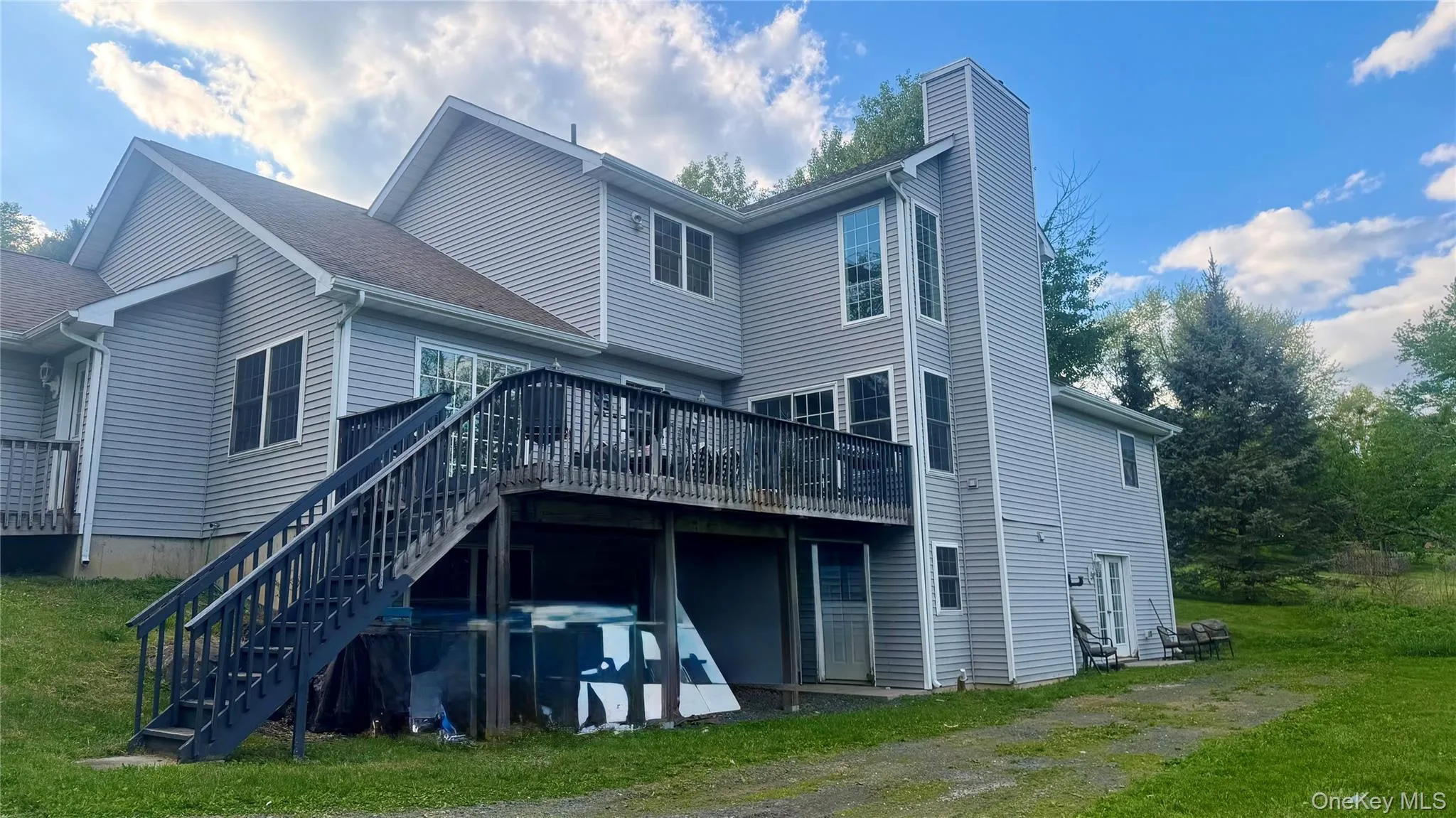 Multi-level exterior with light gray siding, an expansive upper deck with stairs, a prominent chimney, and multiple windows Multi-level exterior with light gray siding, an expansive upper deck with stairs, a prominent chimney, and multiple windows