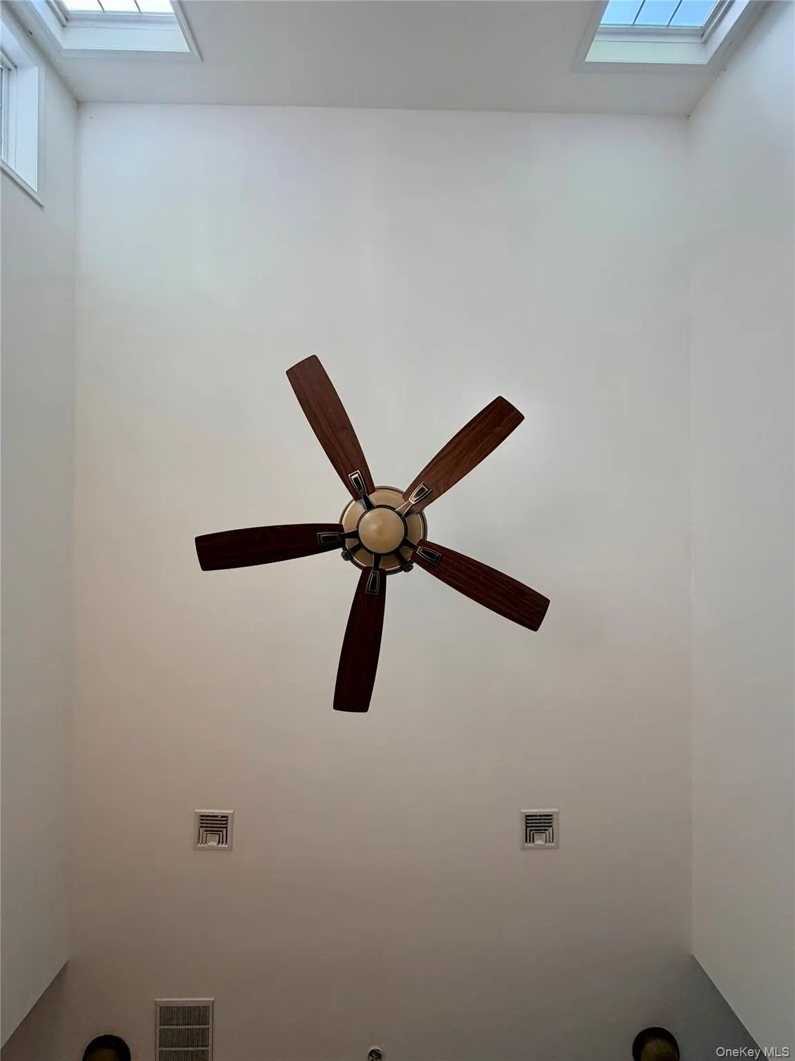 Vaulted ceiling featuring a ceiling fan with wood-finish blades, two skylights, and high wall windows Vaulted ceiling featuring a ceiling fan with wood-finish blades, two skylights, and high wall windows