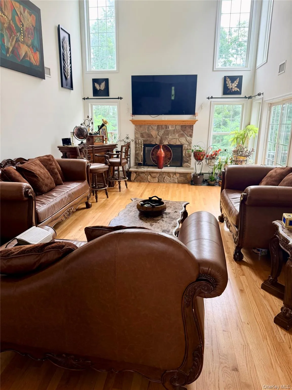Two-story living area featuring hardwood flooring, a stone-clad fireplace, and multiple tall windows Two-story living area featuring hardwood flooring, a stone-clad fireplace, and multiple tall windows