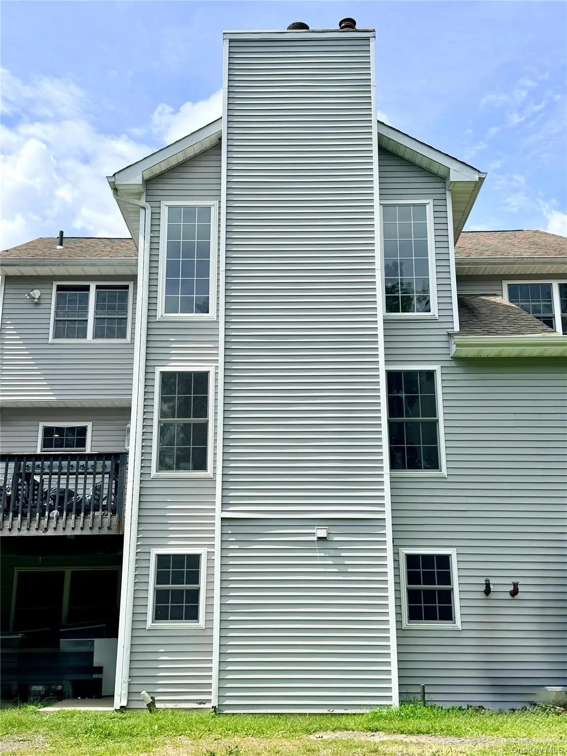 Exterior featuring light grey siding, a prominent chimney, multiple windows with white trim, a multi-level structure. Exterior featuring light grey siding, a prominent chimney, multiple windows with white trim, a multi-level structure.