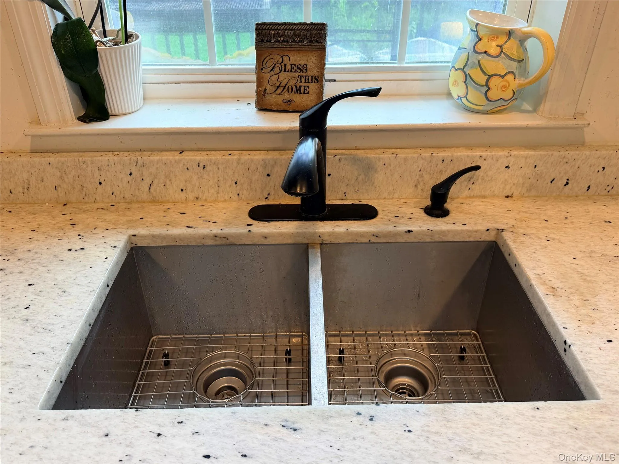 Dual basin undermount sink with stainless steel grates, complemented by a matte black faucet and soap dispenser, set into speckled granite stone countertops with integrated backsplash Dual basin undermount sink with stainless steel grates, complemented by a matte black faucet and soap dispenser, set into speckled granite stone countertops with integrated backsplash