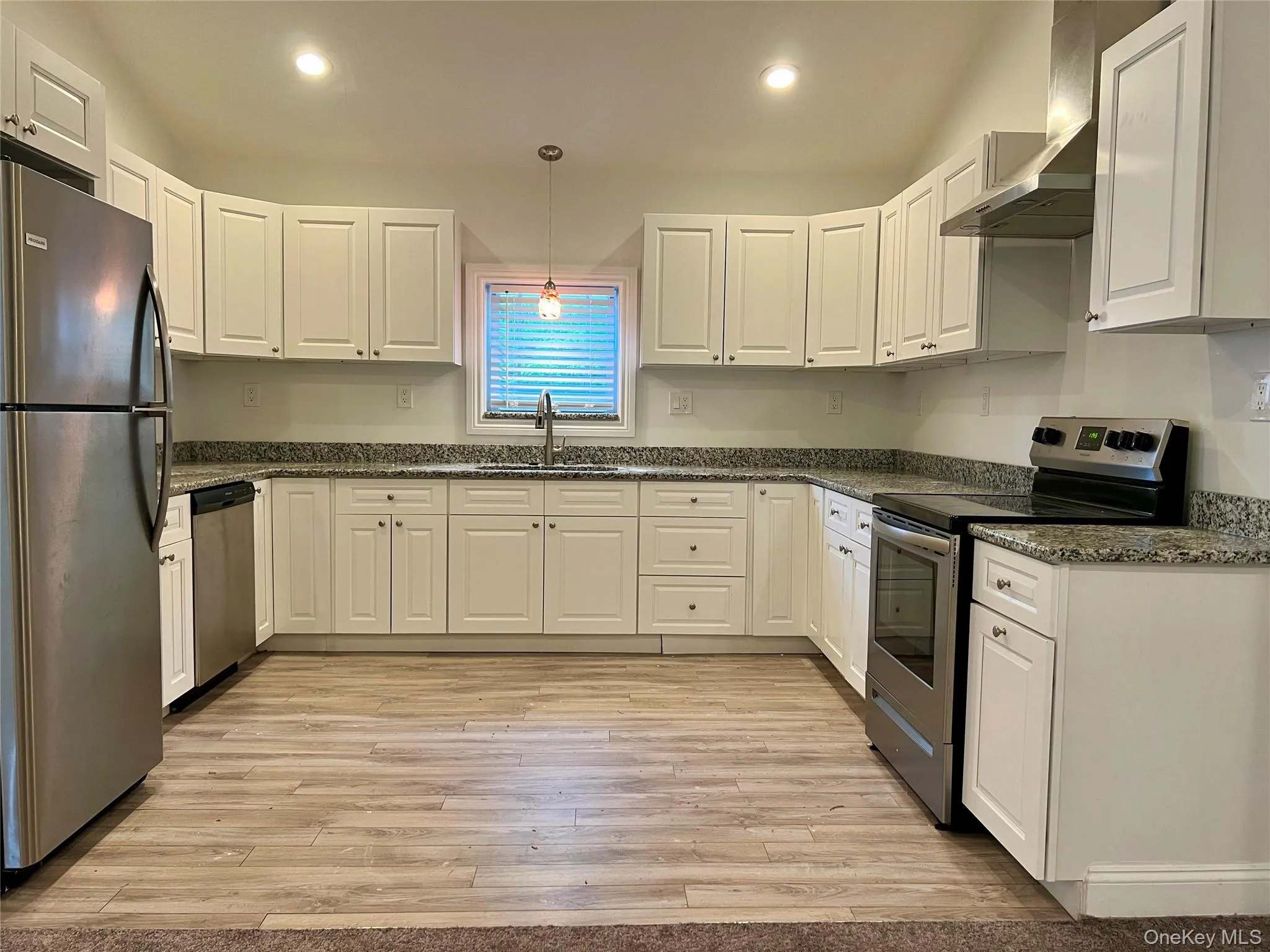 Kitchen with stainless steel appliances, wall chimney exhaust hood, white cabinetry, light wood-type flooring, and recessed lighting Kitchen with stainless steel appliances, wall chimney exhaust hood, white cabinetry, light wood-type flooring, and recessed lighting