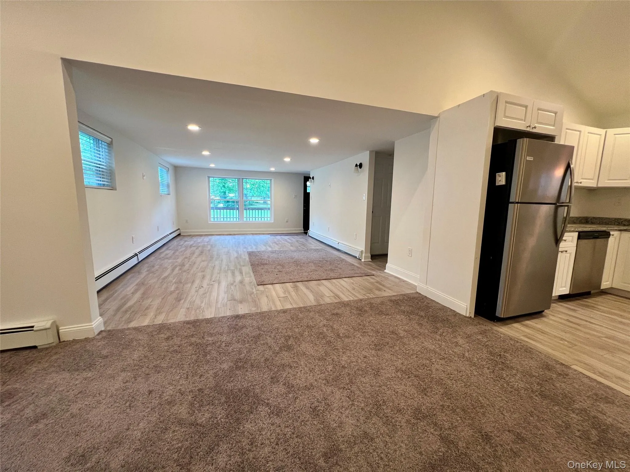 Unfurnished living room with a baseboard heating unit, light wood-style floors, light carpet, and recessed lighting Unfurnished living room with a baseboard heating unit, light wood-style floors, light carpet, and recessed lighting