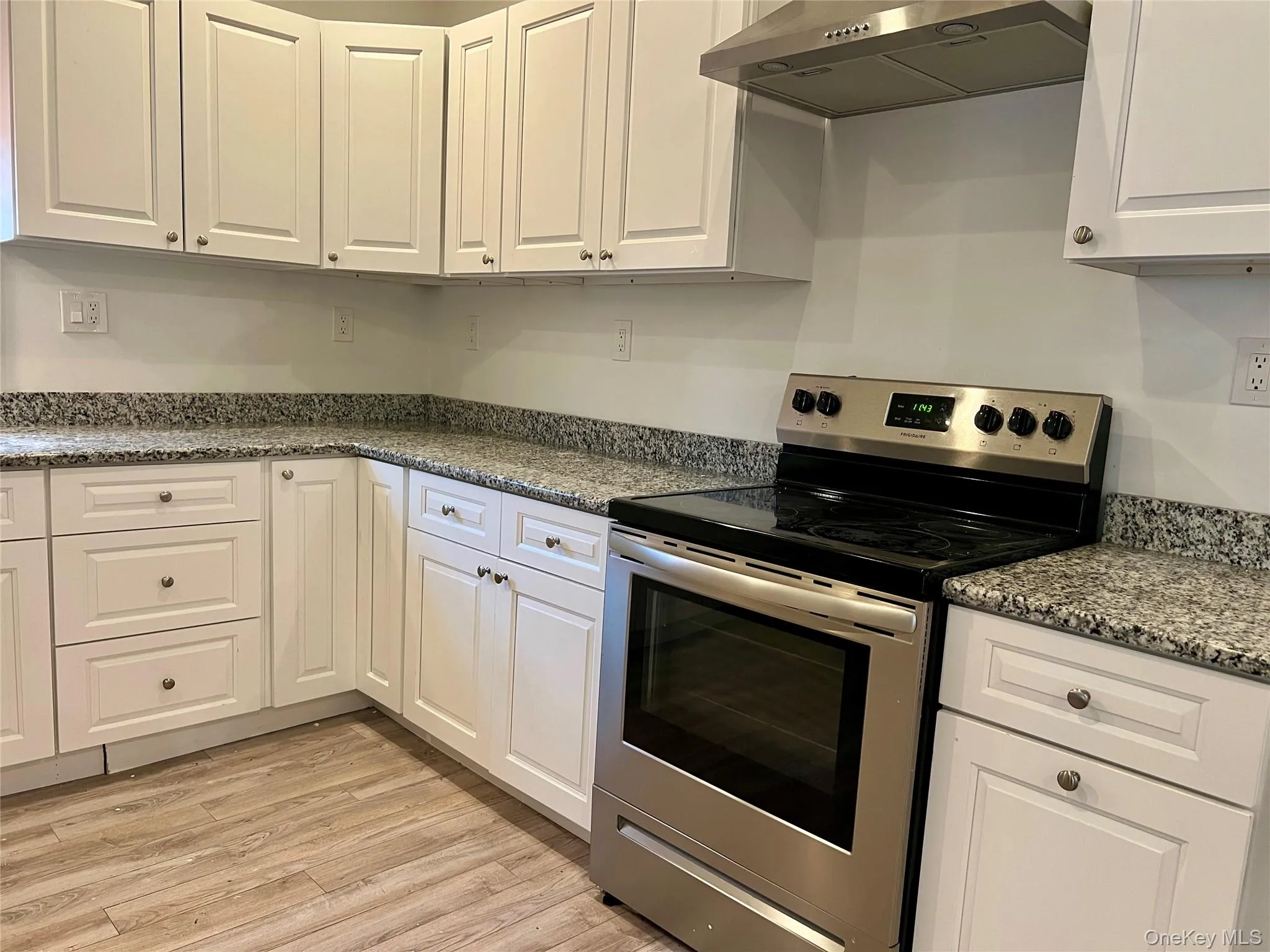 Kitchen with electric range, extractor fan, white cabinets, and light wood finished floors Kitchen with electric range, extractor fan, white cabinets, and light wood finished floors