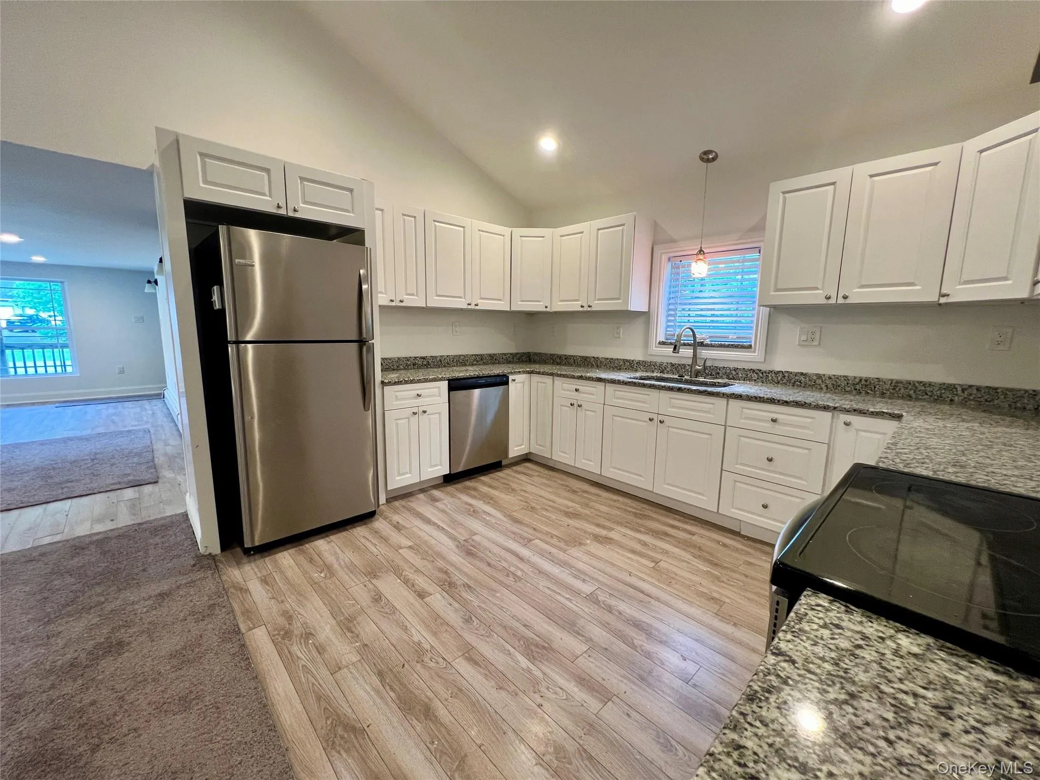 Kitchen featuring stainless steel appliances, light wood-style flooring, white cabinets, recessed lighting, and high vaulted ceiling Kitchen featuring stainless steel appliances, light wood-style flooring, white cabinets, recessed lighting, and high vaulted ceiling
