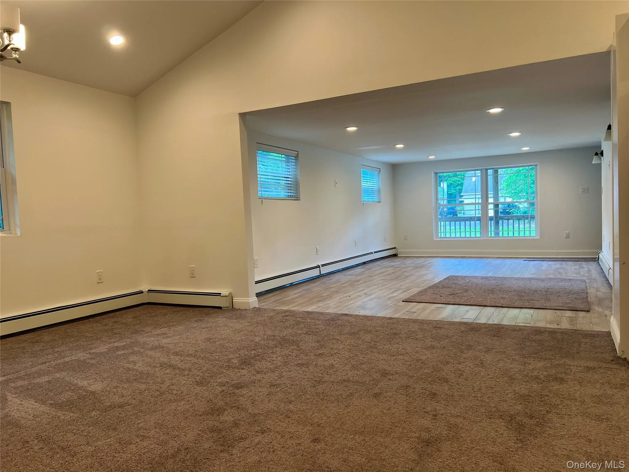 Empty room with a baseboard heating unit, recessed lighting, vaulted ceiling, wood finished floors, and carpet floors Empty room with a baseboard heating unit, recessed lighting, vaulted ceiling, wood finished floors, and carpet floors