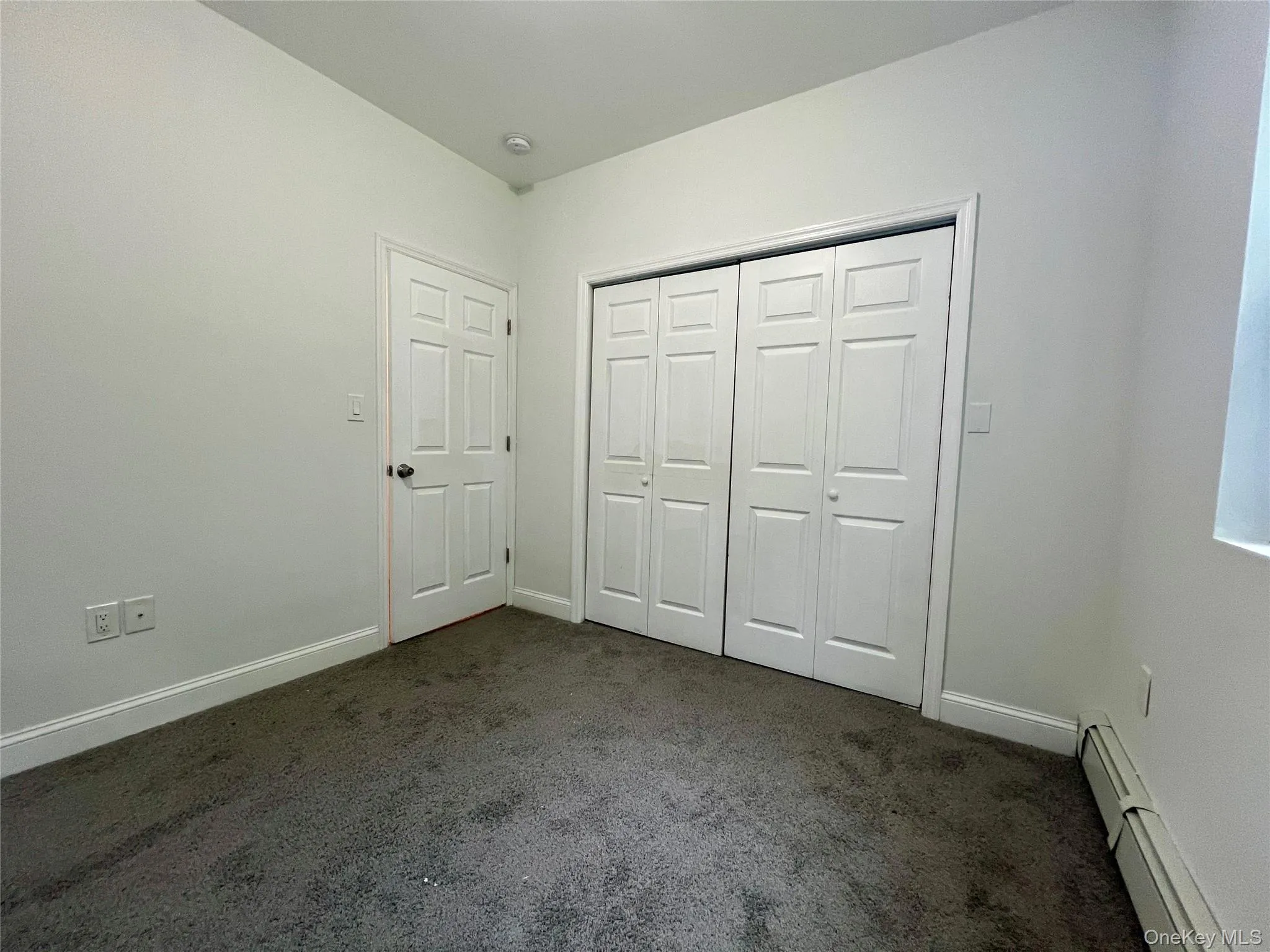 Unfurnished bedroom featuring a baseboard heating unit, dark colored carpet, and a closet Unfurnished bedroom featuring a baseboard heating unit, dark colored carpet, and a closet