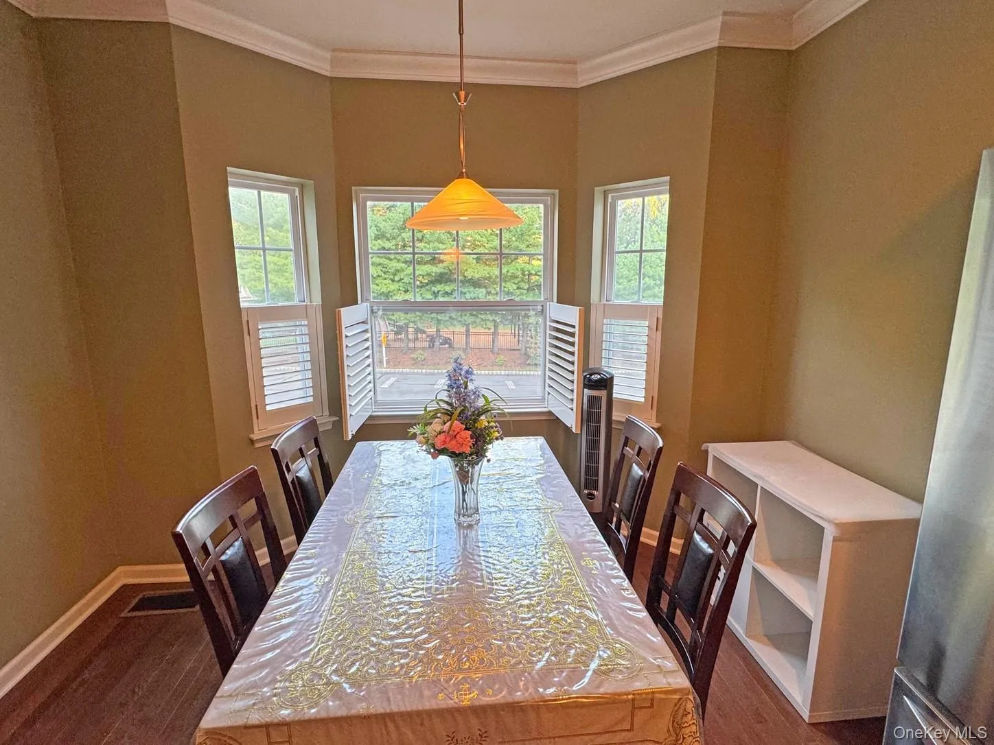 Bay window with internal plantation shutters, crown molding, wood-finish flooring, and a built-in shelving unit Bay window with internal plantation shutters, crown molding, wood-finish flooring, and a built-in shelving unit