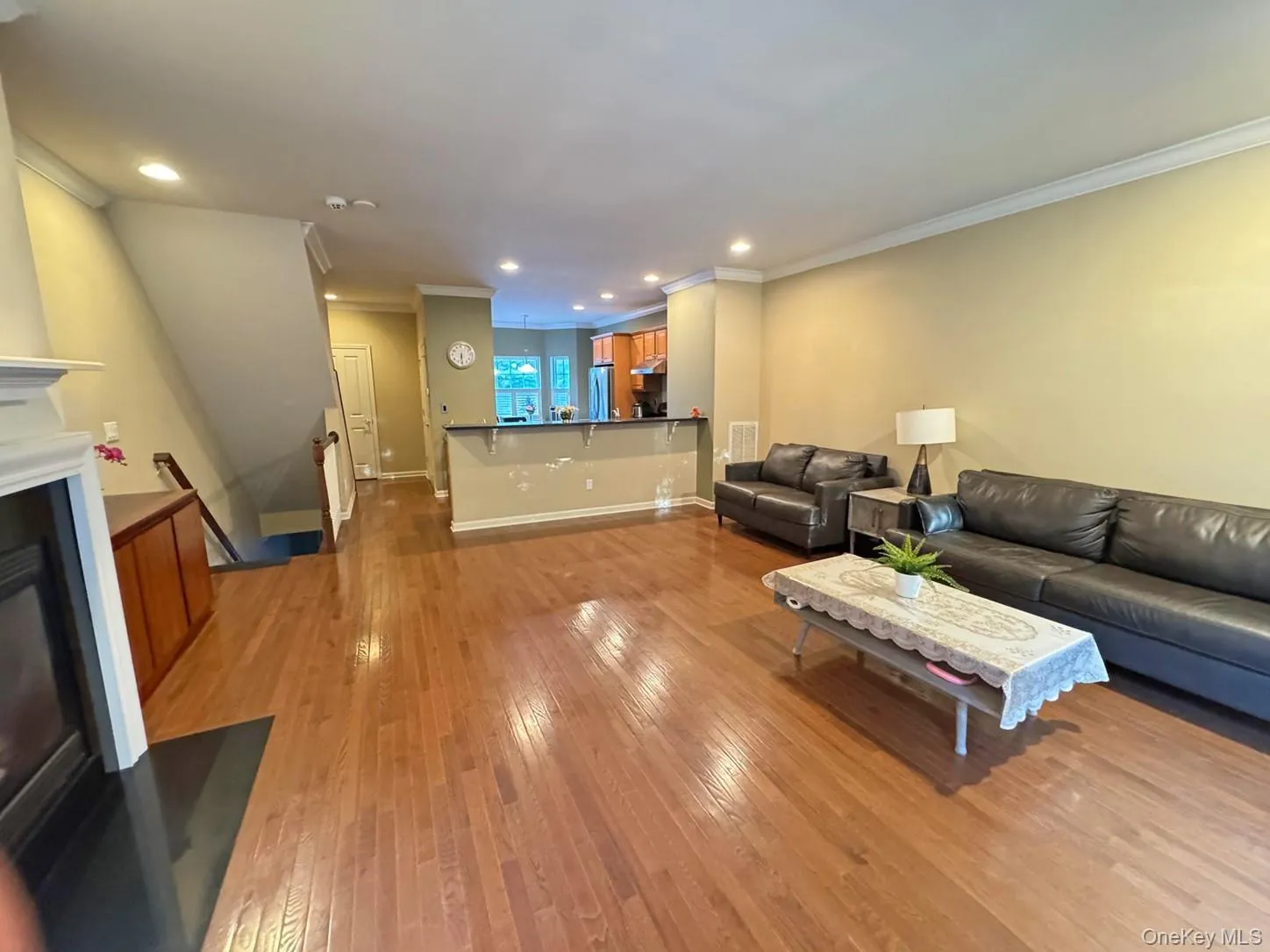 Hardwood flooring, recessed lighting, crown molding, built-in fireplace, and a partial view of the kitchen with a breakfast bar Hardwood flooring, recessed lighting, crown molding, built-in fireplace, and a partial view of the kitchen with a breakfast bar