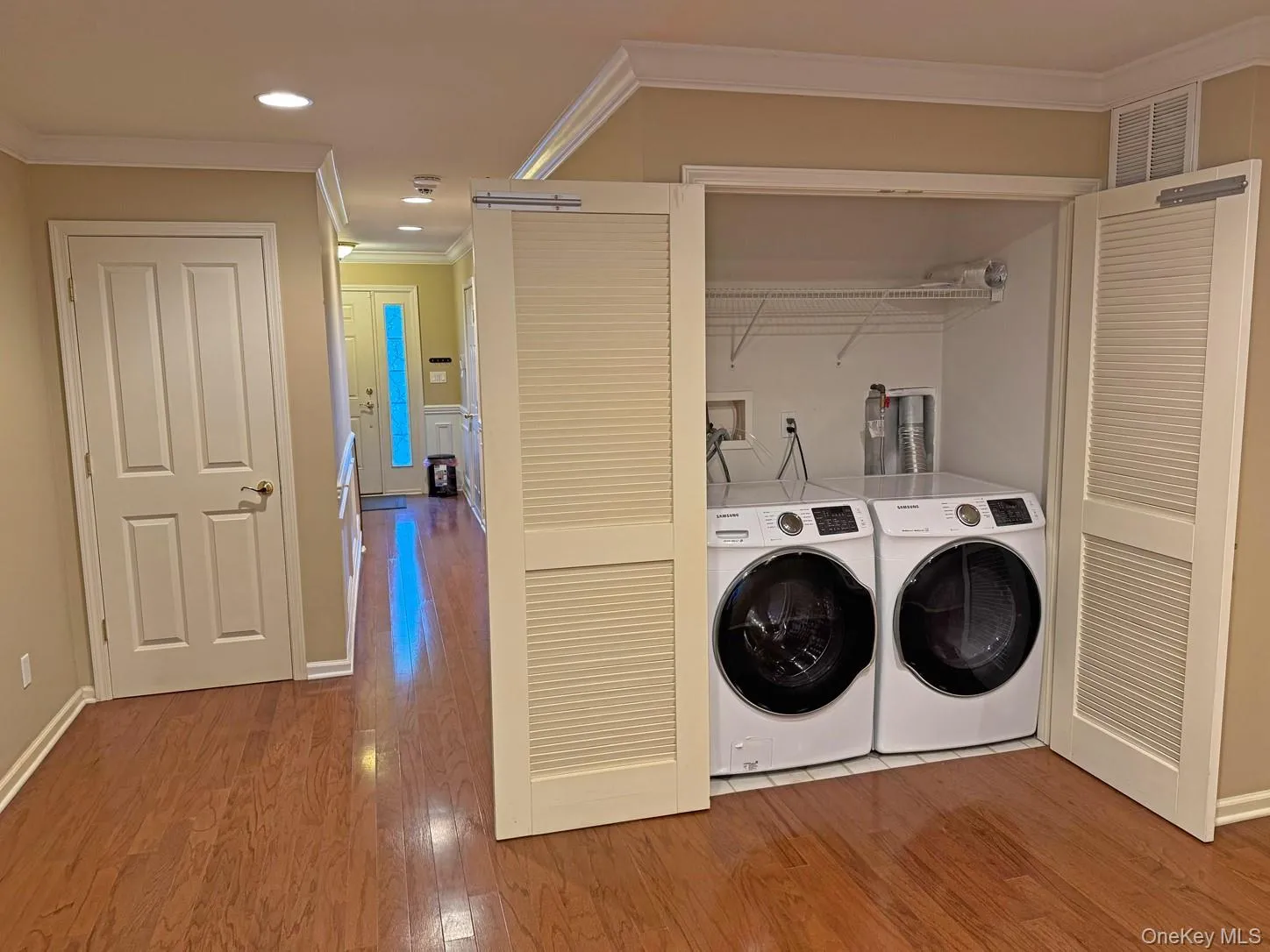 Wood-finish flooring throughout, featuring a recessed lighting, crown molding, and a dedicated laundry closet with louvered bifold doors Wood-finish flooring throughout, featuring a recessed lighting, crown molding, and a dedicated laundry closet with louvered bifold doors