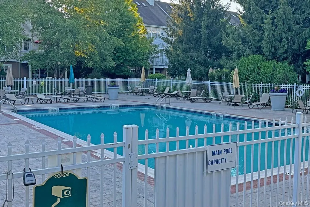 Outdoor swimming pool featuring a white perimeter fence, paved pool deck, and surrounding mature trees Outdoor swimming pool featuring a white perimeter fence, paved pool deck, and surrounding mature trees
