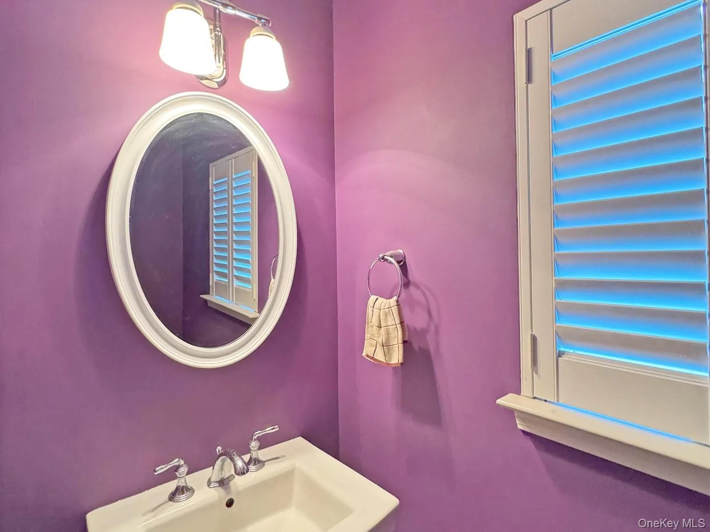 Pedestal sink with chrome faucet, framed oval mirror, and wall-mounted vanity lighting Pedestal sink with chrome faucet, framed oval mirror, and wall-mounted vanity lighting