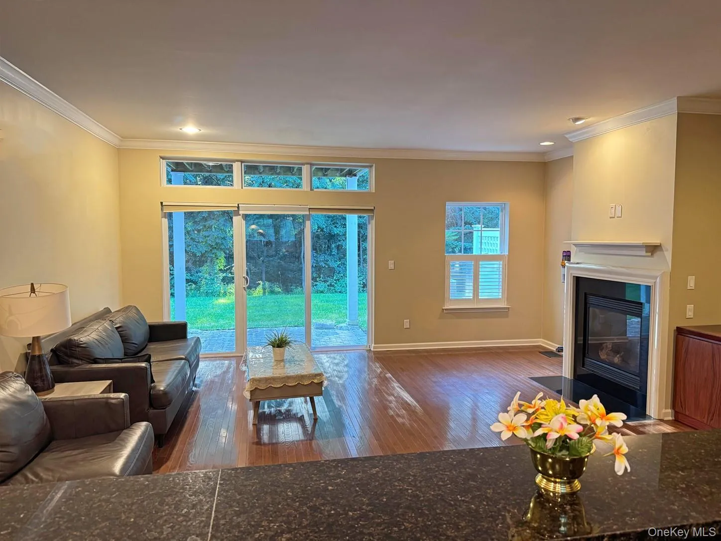Wood-finish flooring throughout, featuring a fireplace with a white mantel, sliding glass doors to the exterior, and a built-in window with horizontal blinds Wood-finish flooring throughout, featuring a fireplace with a white mantel, sliding glass doors to the exterior, and a built-in window with horizontal blinds