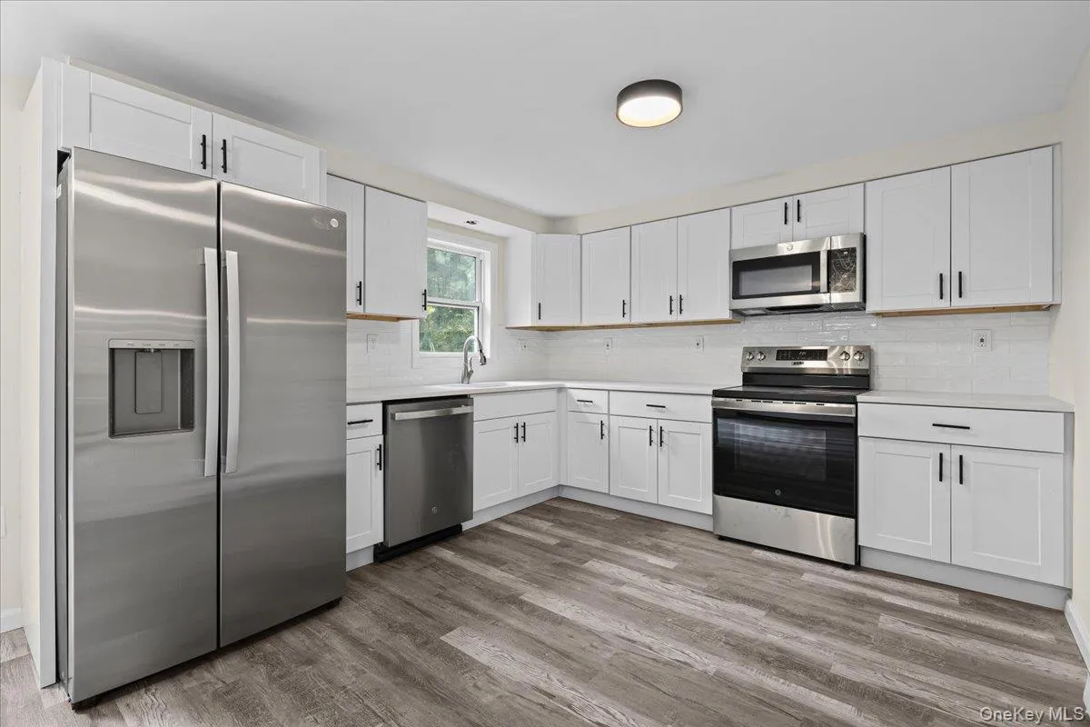 Spacious Kitchen Showcasing White Cabinetry, Large Quartzite Counter with Stainless Appliances Spacious Kitchen Showcasing White Cabinetry, Large Quartzite Counter with Stainless Appliances