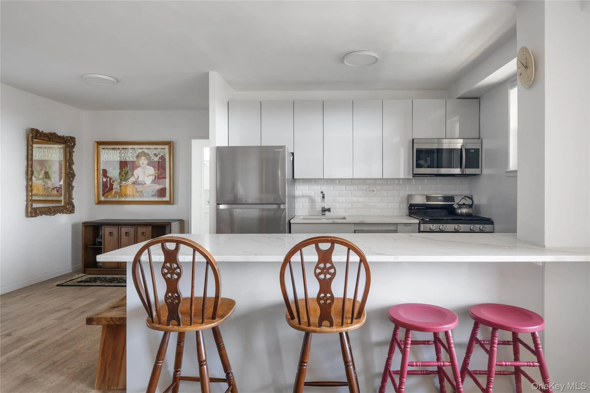 Open-concept kitchen with white shaker-style cabinetry, stainless steel appliances, white subway tile backsplash, and a white countertop with breakfast bar seating Open-concept kitchen with white shaker-style cabinetry, stainless steel appliances, white subway tile backsplash, and a white countertop with breakfast bar seating