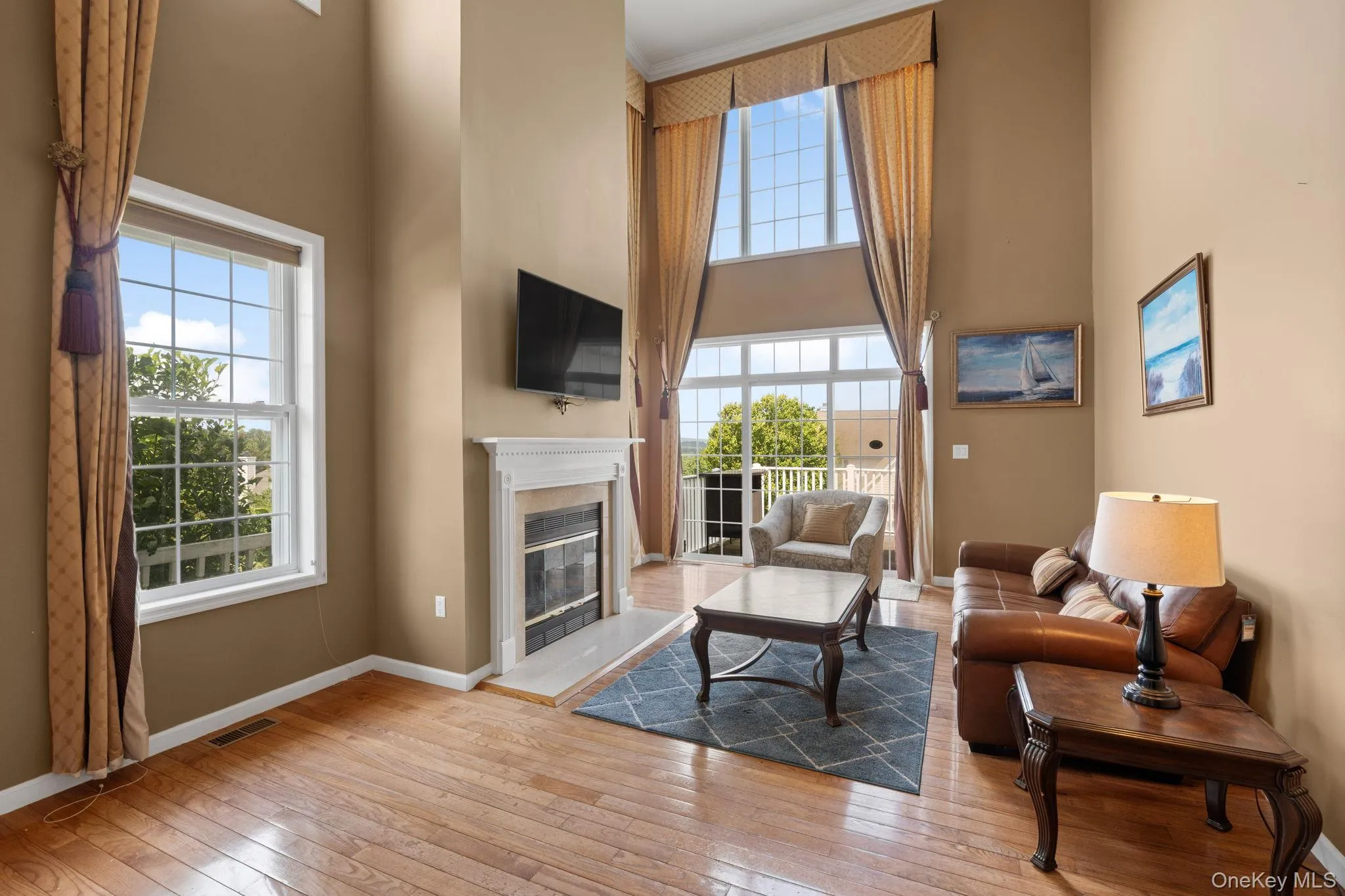Living area with a towering ceiling, wood-type flooring, healthy amount of natural light, and a glass covered fireplace Living area with a towering ceiling, wood-type flooring, healthy amount of natural light, and a glass covered fireplace