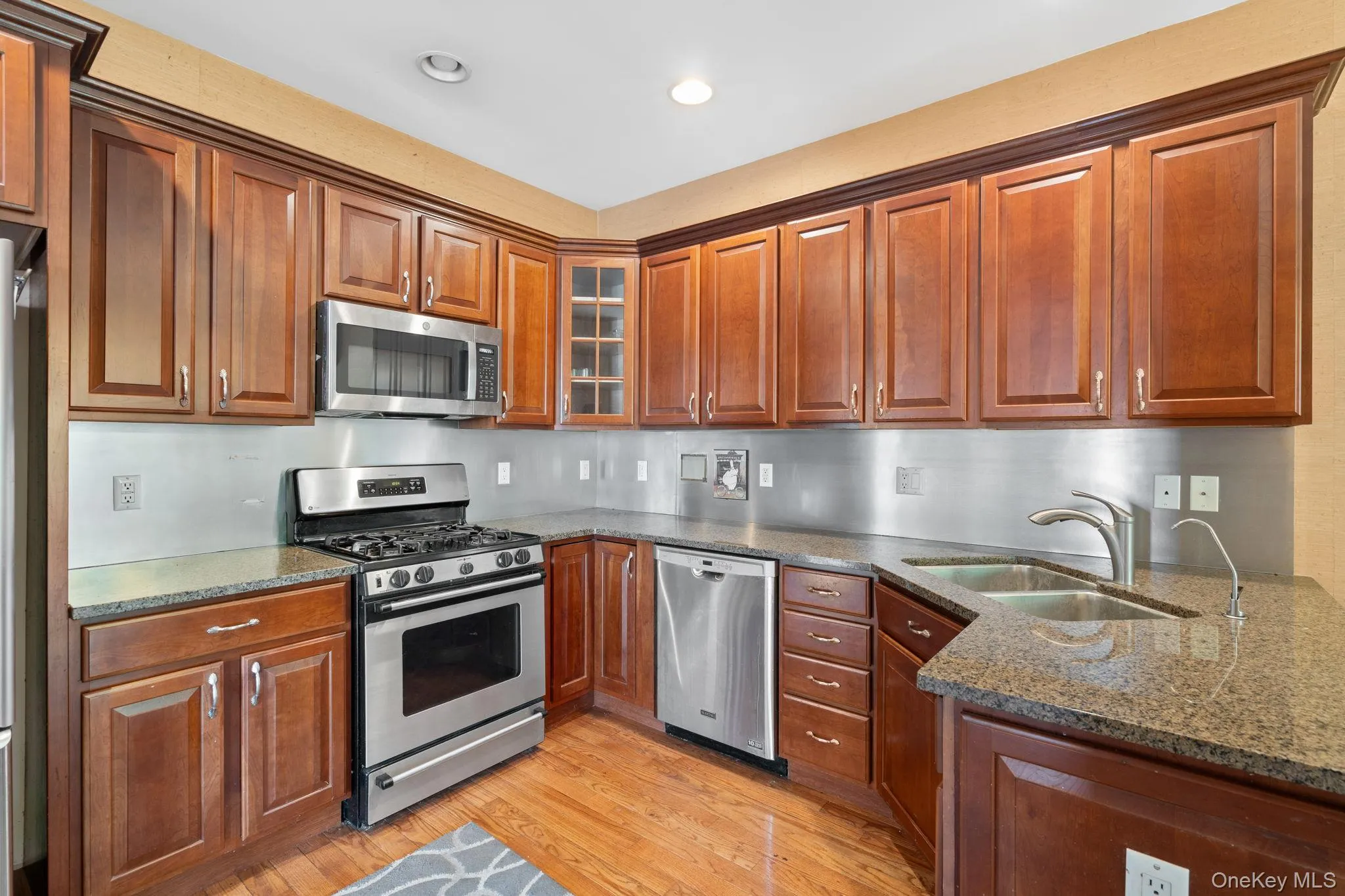 Kitchen featuring appliances with stainless steel finishes, dark stone counters, light wood-style flooring, brown cabinetry, and recessed lighting Kitchen featuring appliances with stainless steel finishes, dark stone counters, light wood-style flooring, brown cabinetry, and recessed lighting