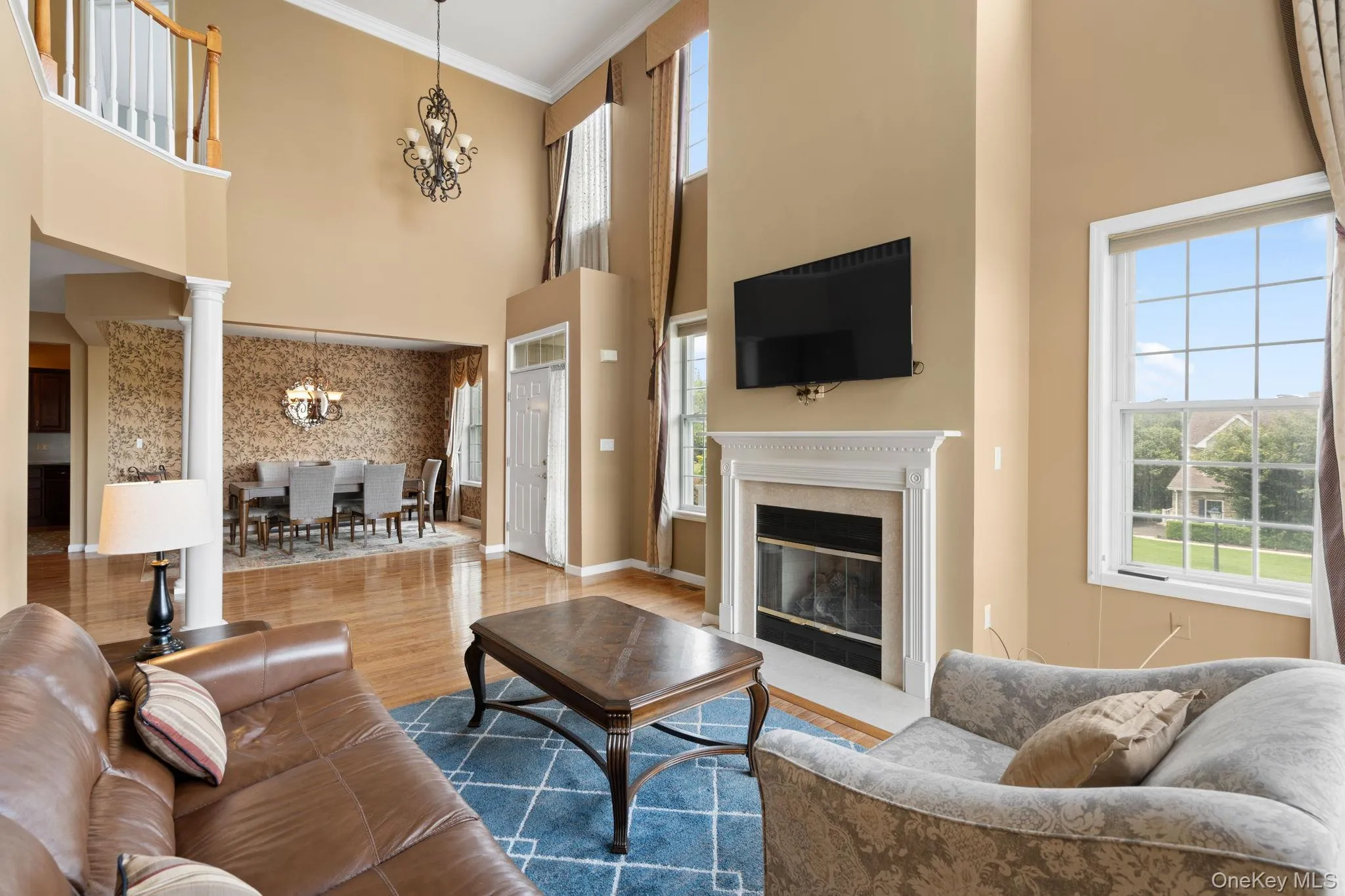 Living room featuring a chandelier, plenty of natural light, a high ceiling, ornamental molding, and wood finished floors Living room featuring a chandelier, plenty of natural light, a high ceiling, ornamental molding, and wood finished floors
