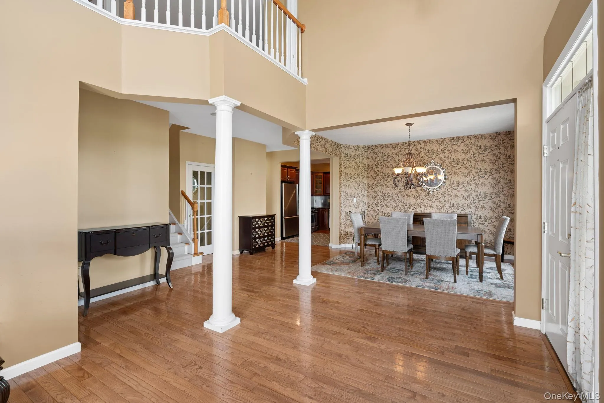 Dining area featuring ornate columns, wood finished floors, a towering ceiling, a chandelier, and stairway Dining area featuring ornate columns, wood finished floors, a towering ceiling, a chandelier, and stairway