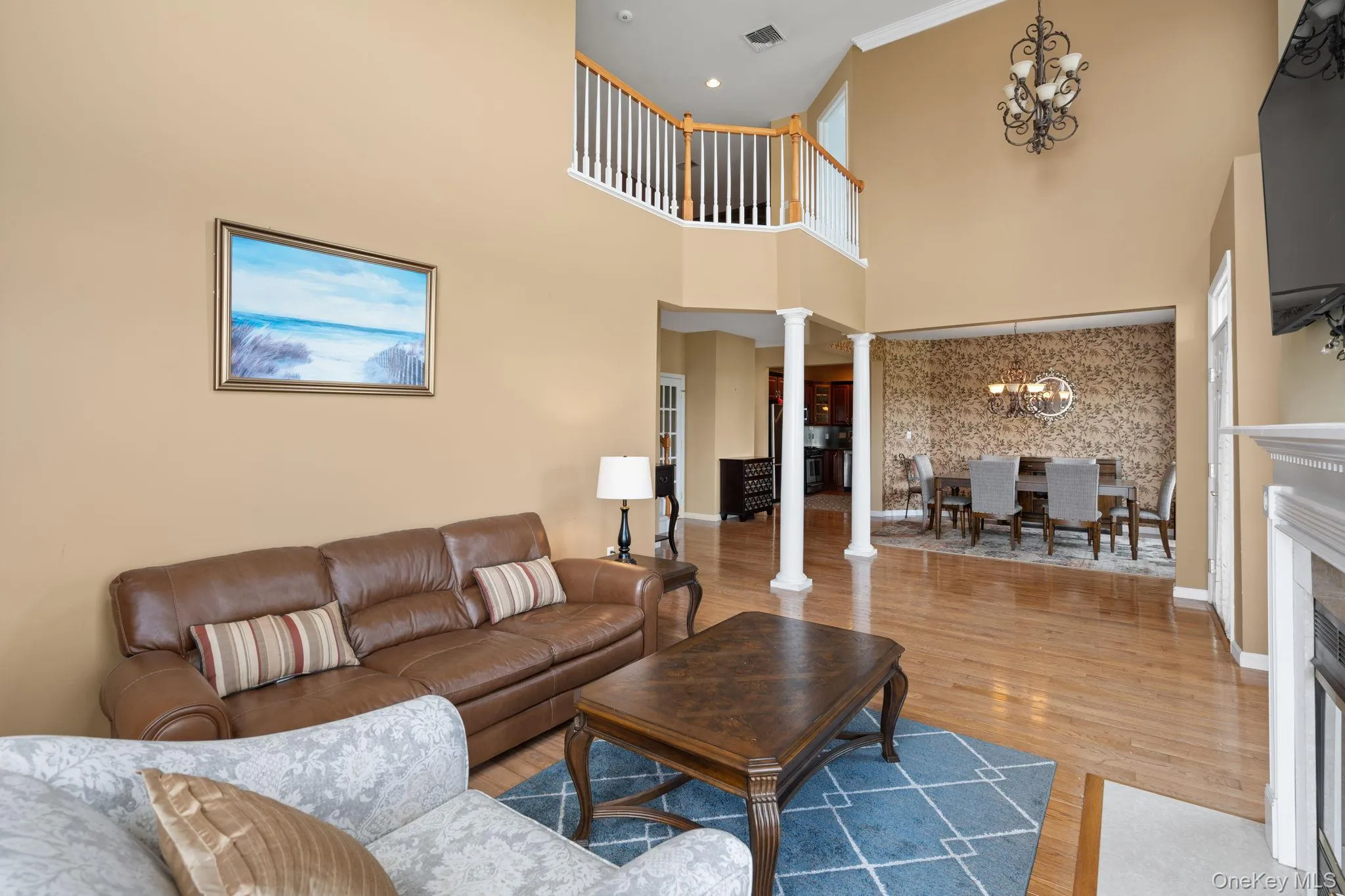 Living area with ornate columns, a chandelier, wood finished floors, a towering ceiling, and a fireplace with flush hearth Living area with ornate columns, a chandelier, wood finished floors, a towering ceiling, and a fireplace with flush hearth
