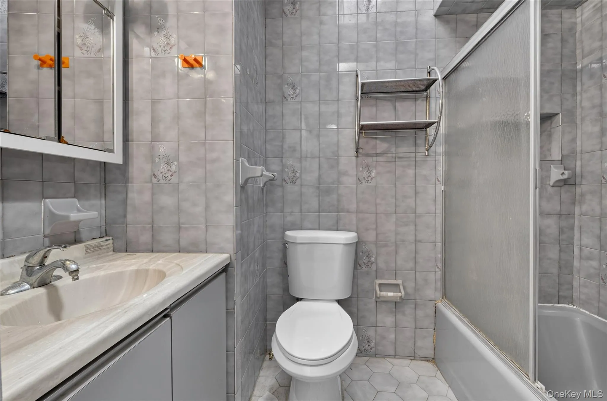 Light gray tile walls, vanity with integrated sink, mirrored medicine cabinet, toilet, and a shower-tub combination with sliding glass doors Light gray tile walls, vanity with integrated sink, mirrored medicine cabinet, toilet, and a shower-tub combination with sliding glass doors