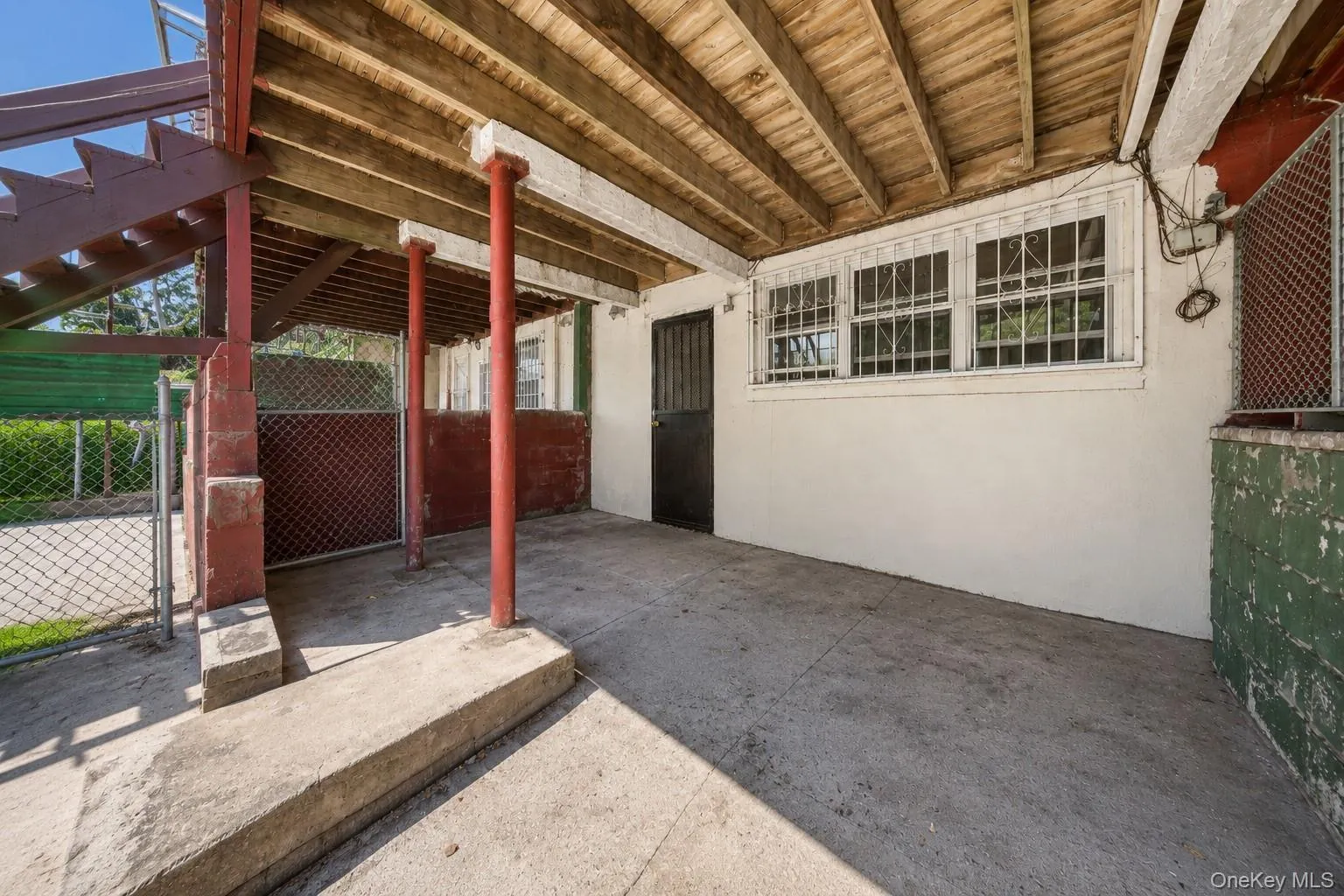 Covered concrete patio with exposed wood ceiling beams and multiple windows featuring security bars Covered concrete patio with exposed wood ceiling beams and multiple windows featuring security bars