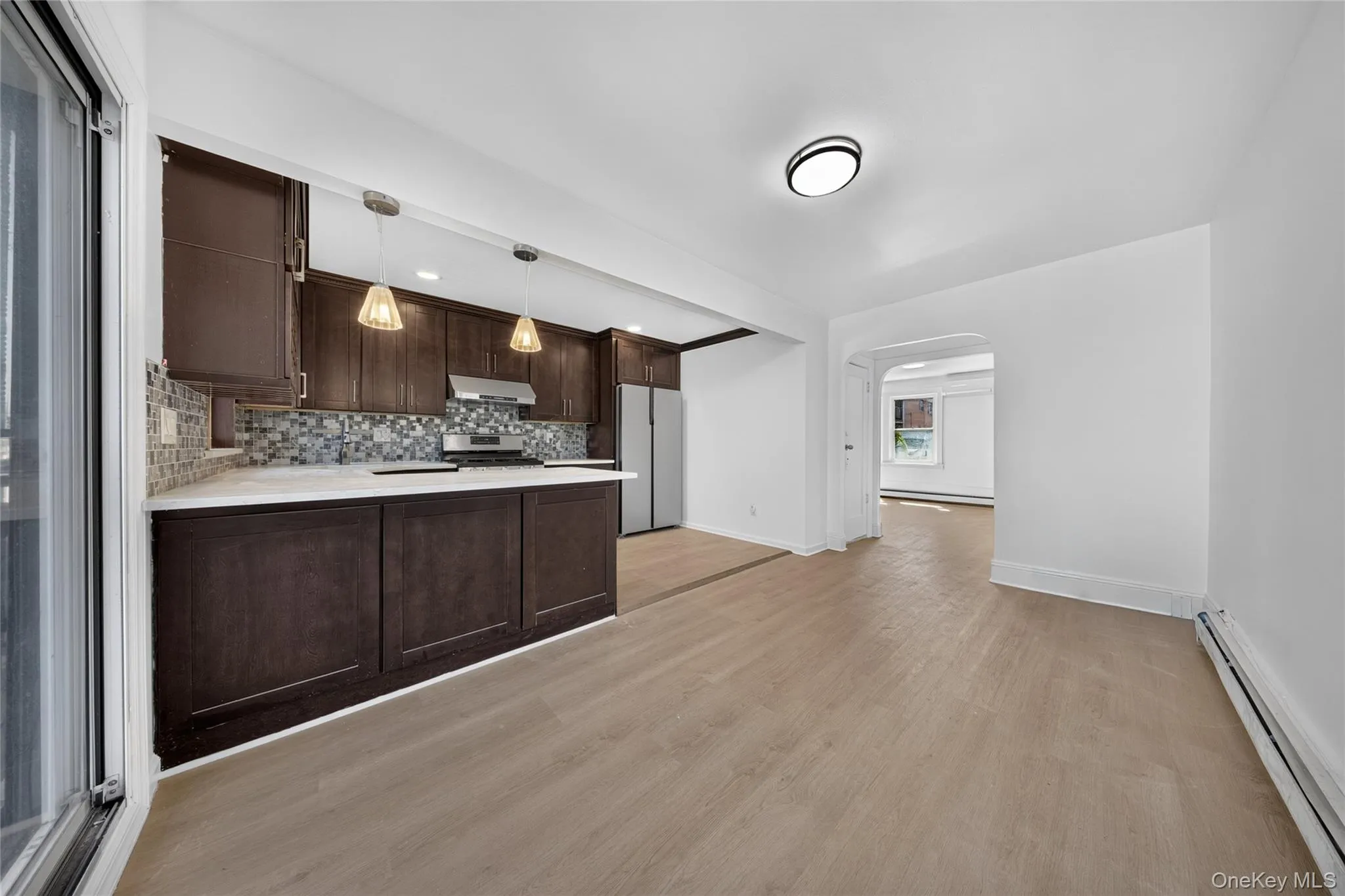 Kitchen featuring dark wood-finish cabinetry, light-colored countertops, a mosaic tile backsplash, and stainless steel appliances Kitchen featuring dark wood-finish cabinetry, light-colored countertops, a mosaic tile backsplash, and stainless steel appliances