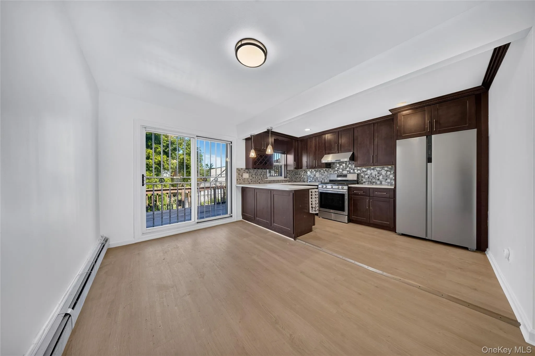 Wood-finish flooring, dark wood cabinetry, a mosaic tile backsplash, and stainless steel appliances Wood-finish flooring, dark wood cabinetry, a mosaic tile backsplash, and stainless steel appliances