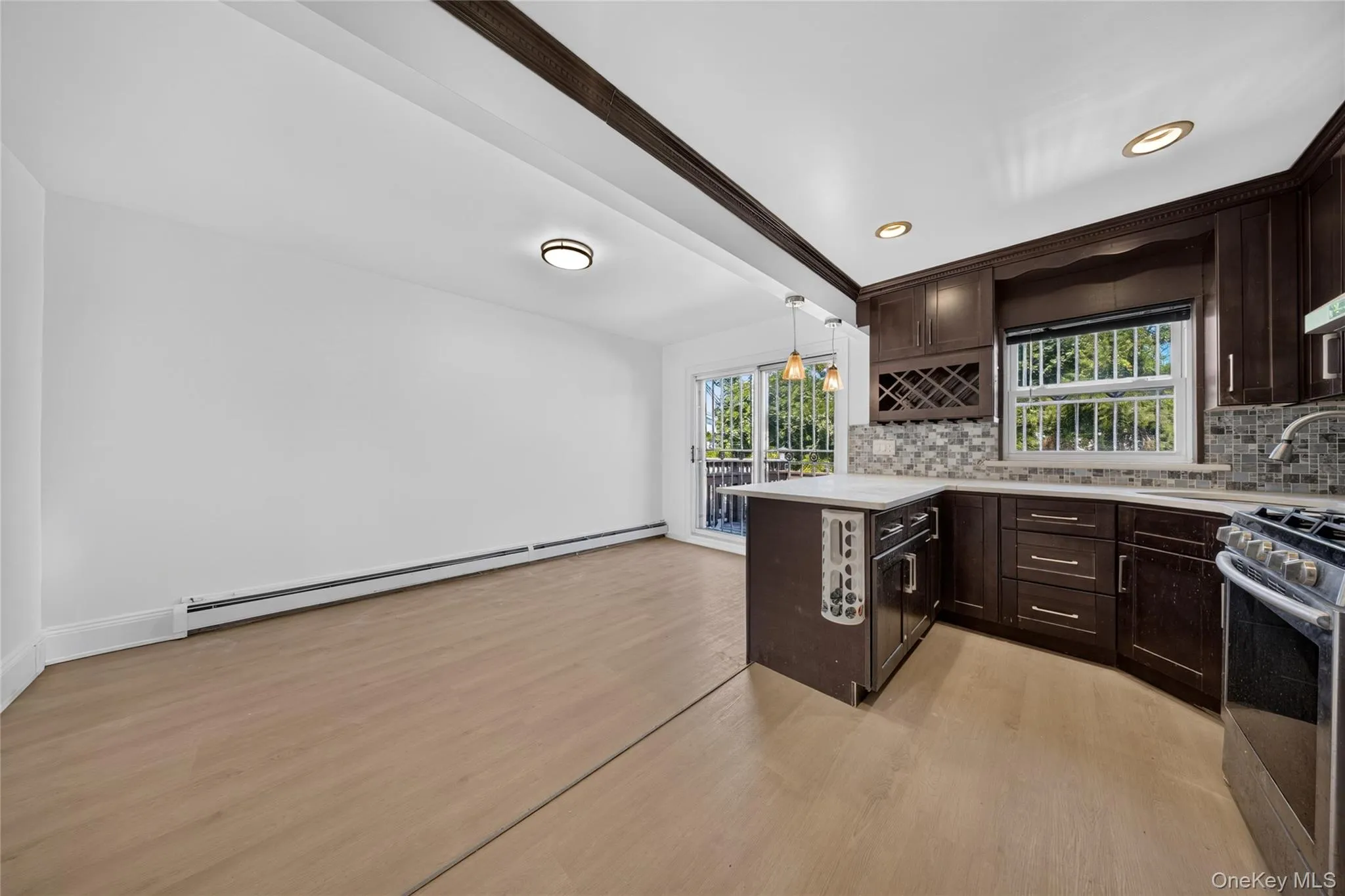 Kitchen featuring wood-finish flooring, dark wood cabinetry, a built-in wine rack, tile backsplash, and a sliding glass door to an outdoor deck Kitchen featuring wood-finish flooring, dark wood cabinetry, a built-in wine rack, tile backsplash, and a sliding glass door to an outdoor deck