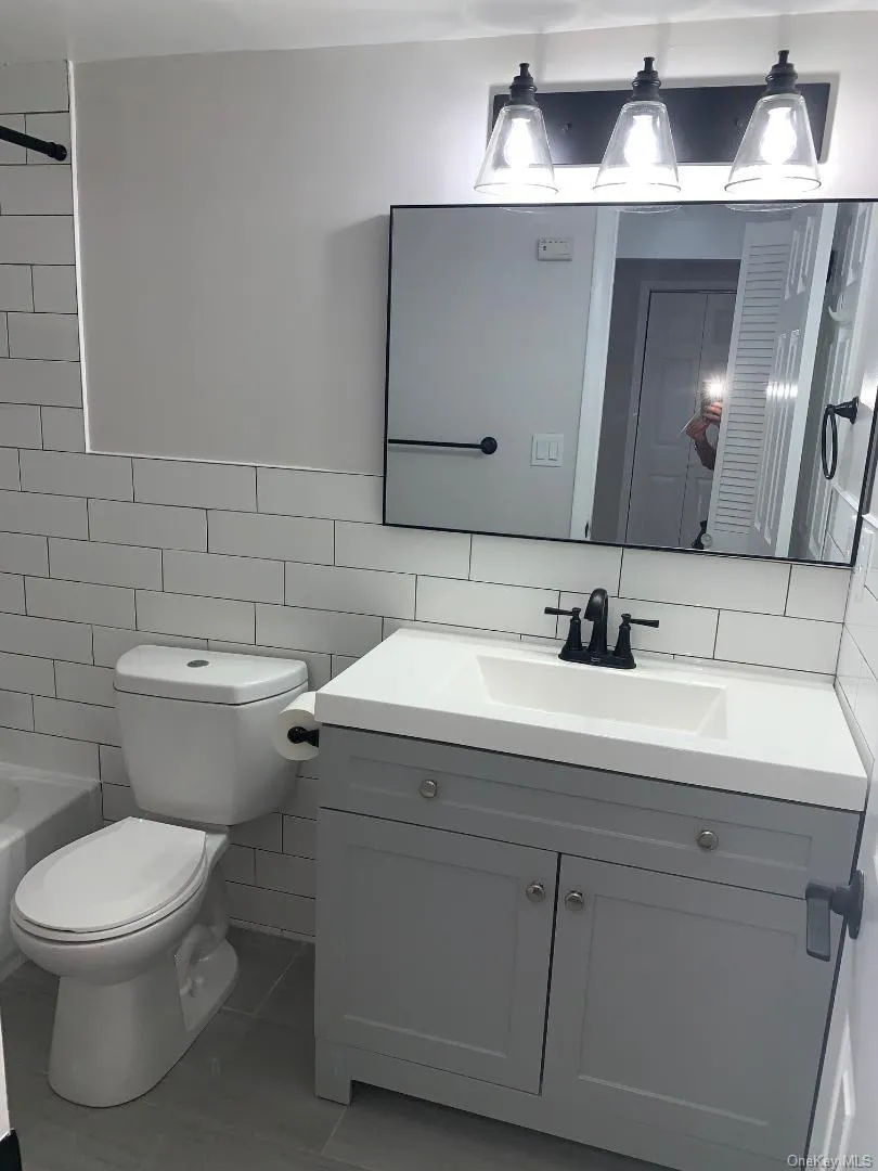 Bathroom featuring vanity, tile walls, tile patterned flooring, and shower / tub combination Bathroom featuring vanity, tile walls, tile patterned flooring, and shower / tub combination
