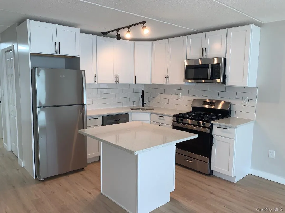 Kitchen with white cabinetry, appliances with stainless steel finishes, quartz counters, decorative backsplash, and light wood-type flooring Kitchen with white cabinetry, appliances with stainless steel finishes, quartz counters, decorative backsplash, and light wood-type flooring