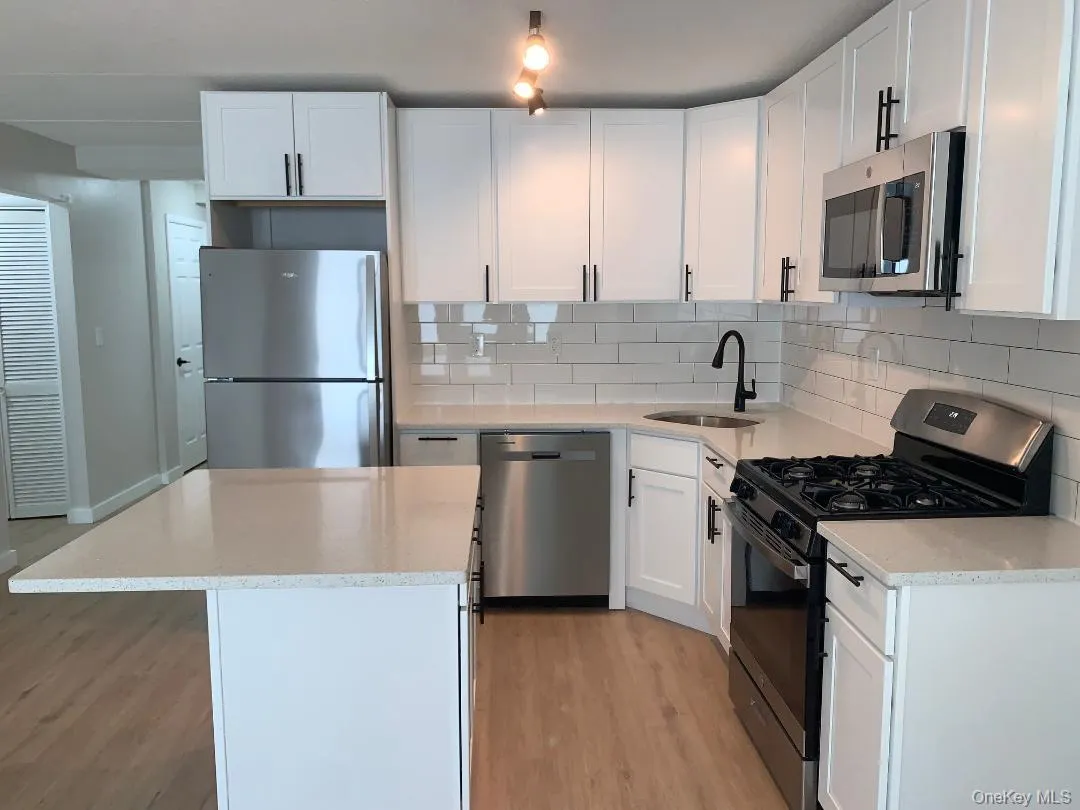 Kitchen featuring stainless steel appliances, light stone countertops, light wood-style flooring, and white cabinets Kitchen featuring stainless steel appliances, light stone countertops, light wood-style flooring, and white cabinets