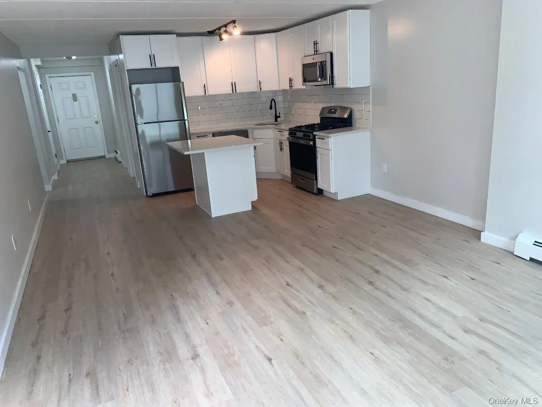 Kitchen with tasteful backsplash, stainless steel appliances, a center island, white cabinetry, and light wood-type flooring Kitchen with tasteful backsplash, stainless steel appliances, a center island, white cabinetry, and light wood-type flooring