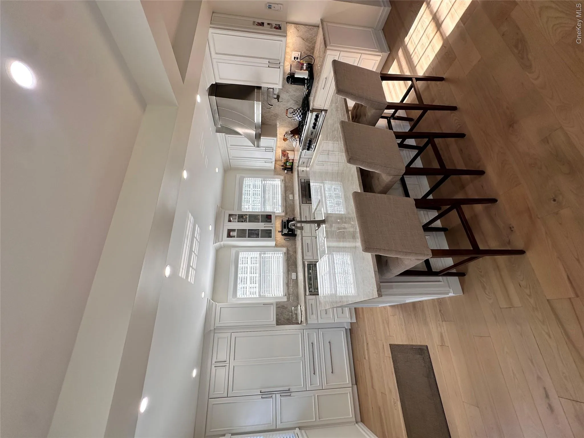 Kitchen featuring light-toned wood-finish flooring, white cabinetry, a large center island with a light-colored countertop, and a stainless steel range hood Kitchen featuring light-toned wood-finish flooring, white cabinetry, a large center island with a light-colored countertop, and a stainless steel range hood
