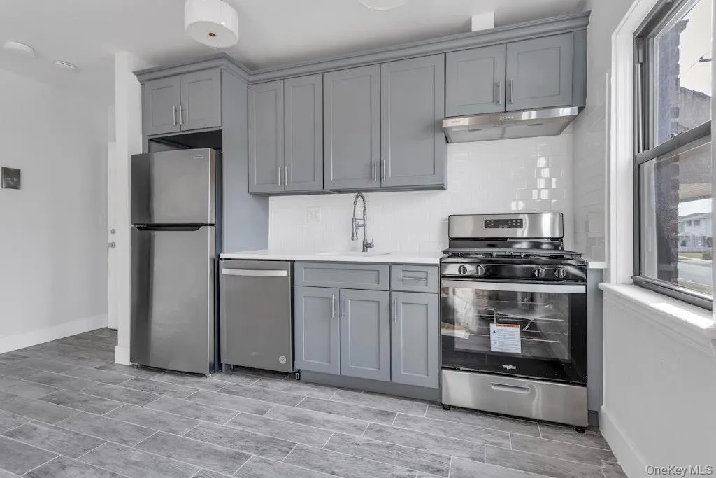 Kitchen with under cabinet range hood, a sink, appliances with stainless steel finishes, backsplash, and gray cabinets Kitchen with under cabinet range hood, a sink, appliances with stainless steel finishes, backsplash, and gray cabinets