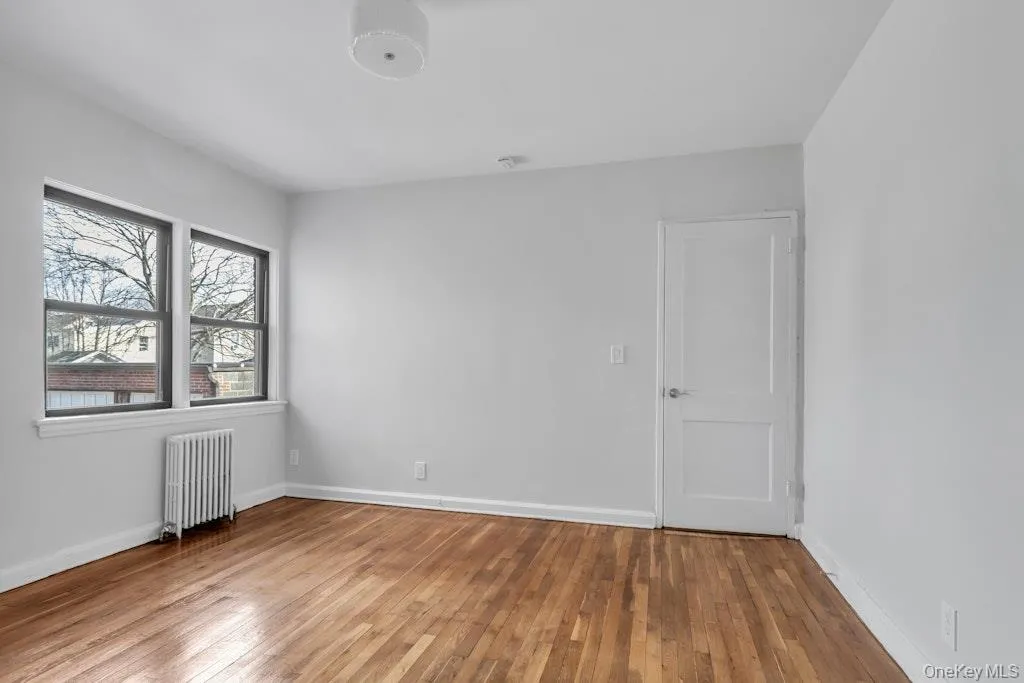 Empty room featuring radiator, hardwood / wood-style flooring, and baseboards Empty room featuring radiator, hardwood / wood-style flooring, and baseboards